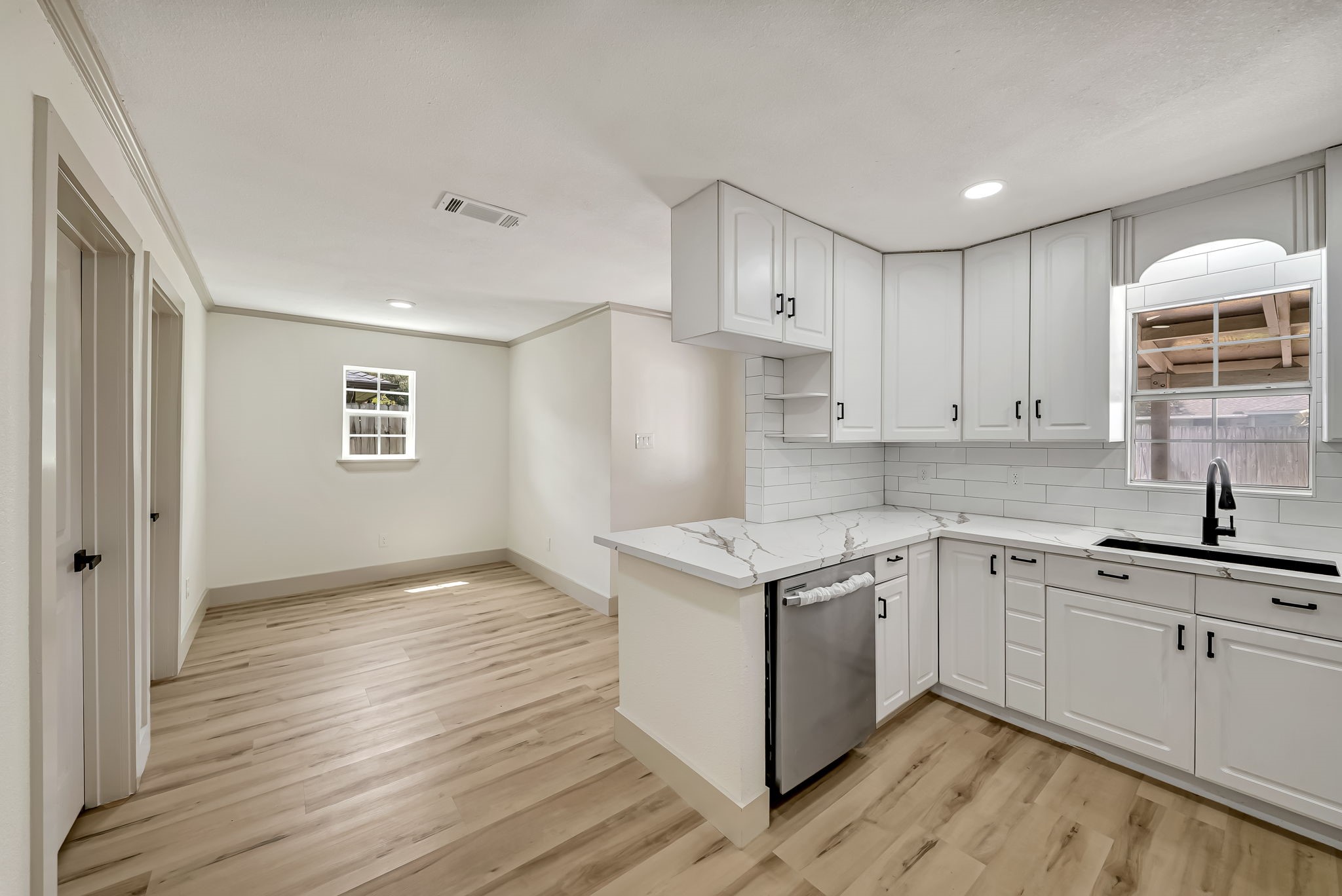 Bright and airy kitchen with modern white cabinetry, sleek marble countertops, and stylish wood flooring, seamlessly flowing into the dinning area.