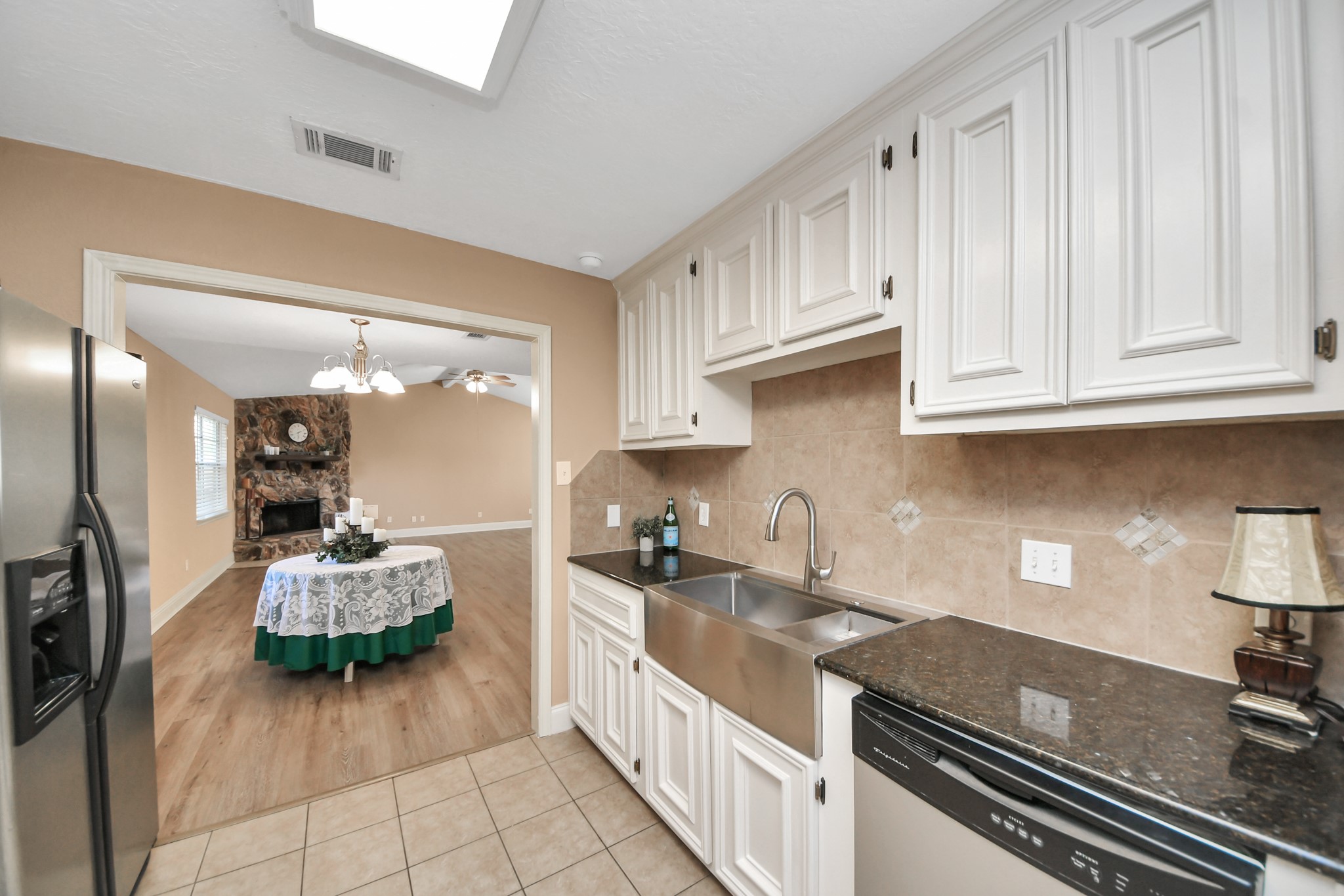 From cooking dinner to hosting memorable gatherings, this kitchens connection to the adjoining dining and living areas makes entertaining convenient. The galley-style layout features white cabinetry, dark countertops, stainless steel appliances, and a distinctive apron-front sink. Just beyond the kitchen, the dining area flows into a spacious living room anchored by a beautiful floor-to-ceiling stone fireplace.