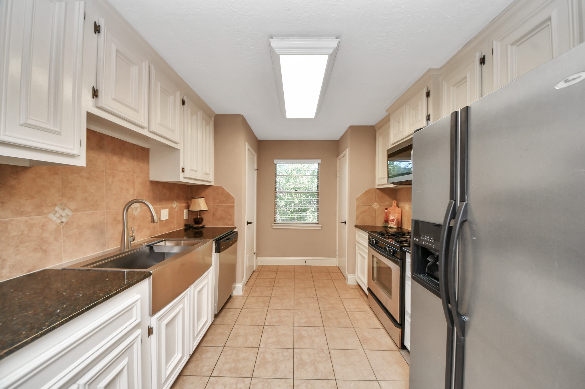 Designed to maximize functionality, this well-appointed galley kitchen offers generous cabinetry and countertop space along both sides of the room. The thoughtful arrangement places the stainless steel farmhouse-style sink and dishwasher opposite the gas range, built-in microwave, and side-by-side refrigerator, creating convenient work areas for cooking and cleanup.