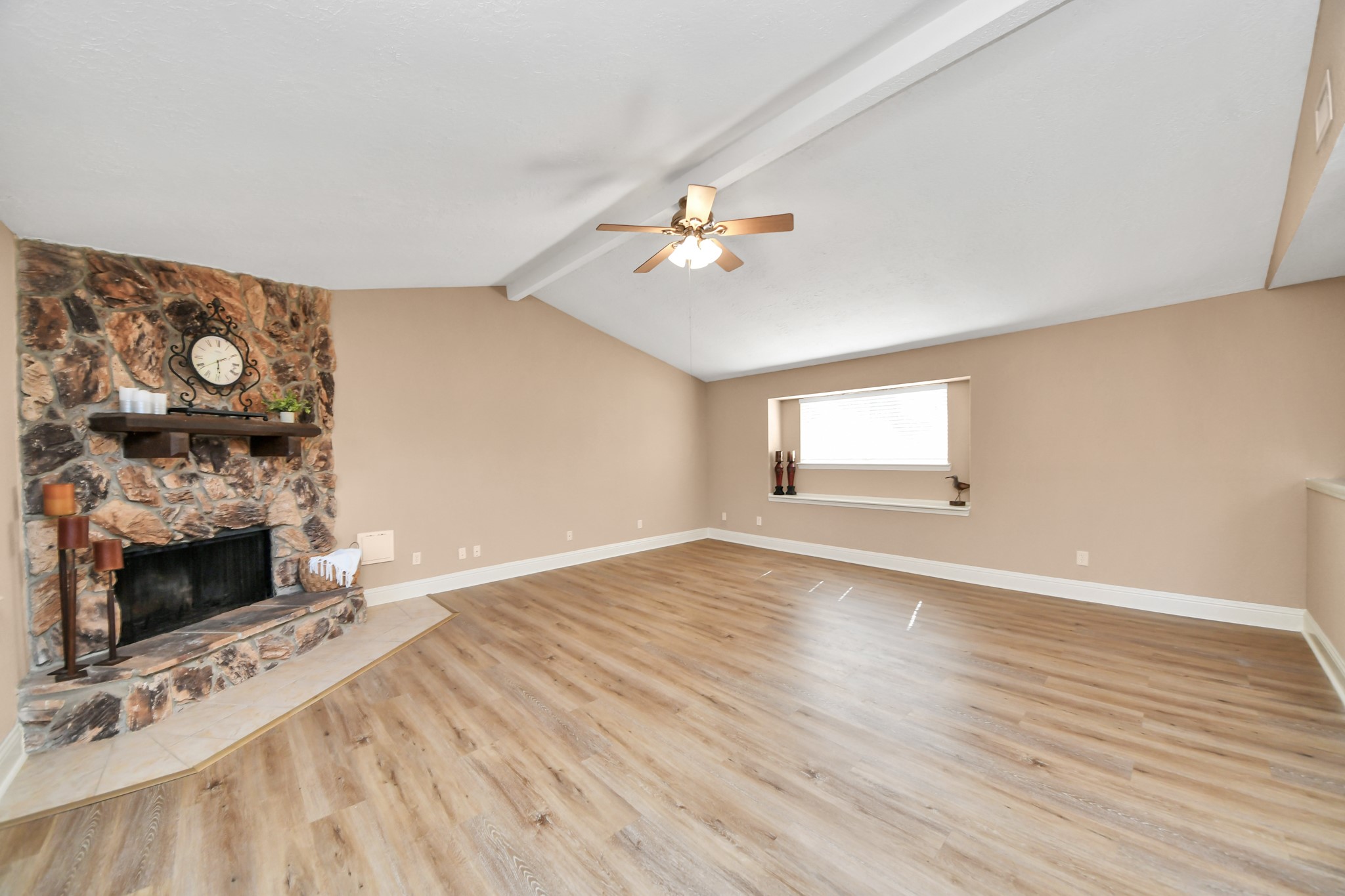 This beautiful living room features a dramatic vaulted ceiling, exposed beam detail, and a striking natural stone fireplace.