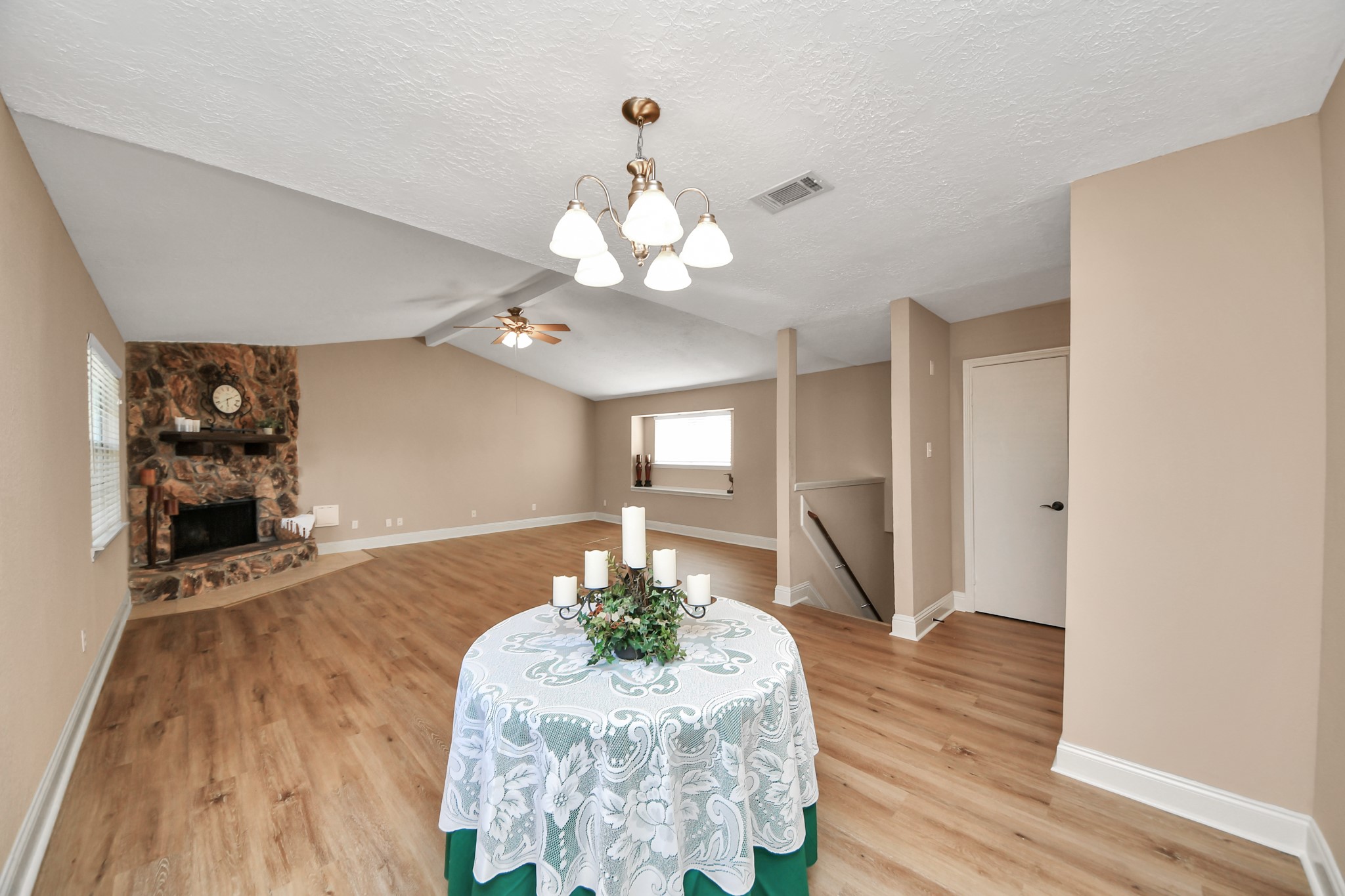 This inviting living and dining space offers an open, flowing layout with beautiful wood-look flooring, neutral tones, and abundant room to gather. A striking floor-to-ceiling stone fireplace anchors the living area, while the adjoining dining space creates an ideal setting for memorable meals and celebrations. The vaulted ceiling adds architectural interest and an airy, expansive feel.
