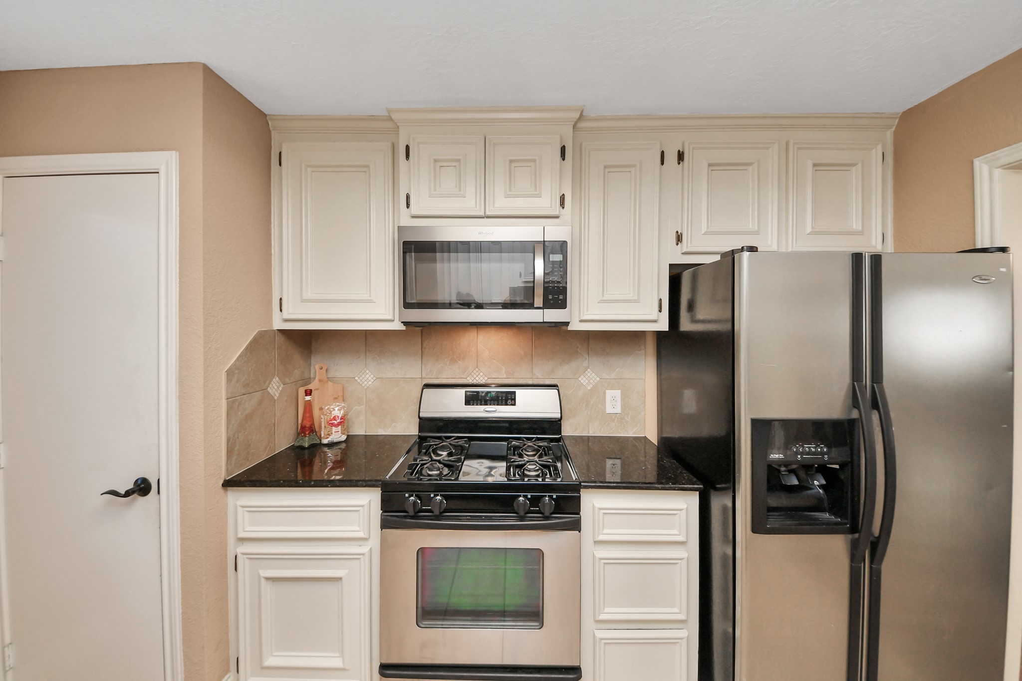 Stainless steel appliances, including a gas range, built-in microwave, and side-by-side refrigerator with an exterior water and ice dispenser, complete the space.