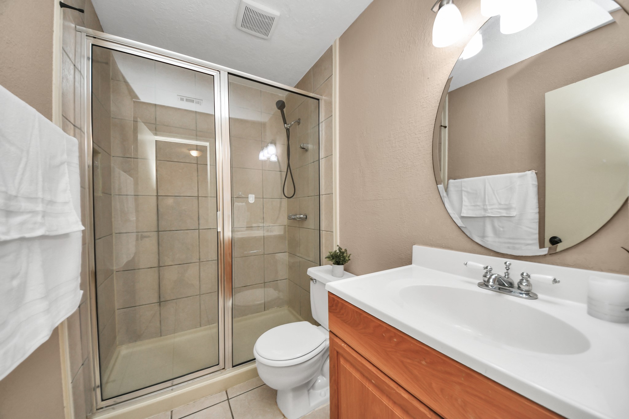 Perfectly positioned between the two first-level secondary bedrooms, this full bathroom offers easy access and everyday functionality. Featuring a spacious glass-enclosed shower with tile surround, a handheld showerhead, an oversized vanity countertop, and a stylish round mirror, this thoughtfully arranged space provides everything needed for a refreshing start or relaxing end to the day