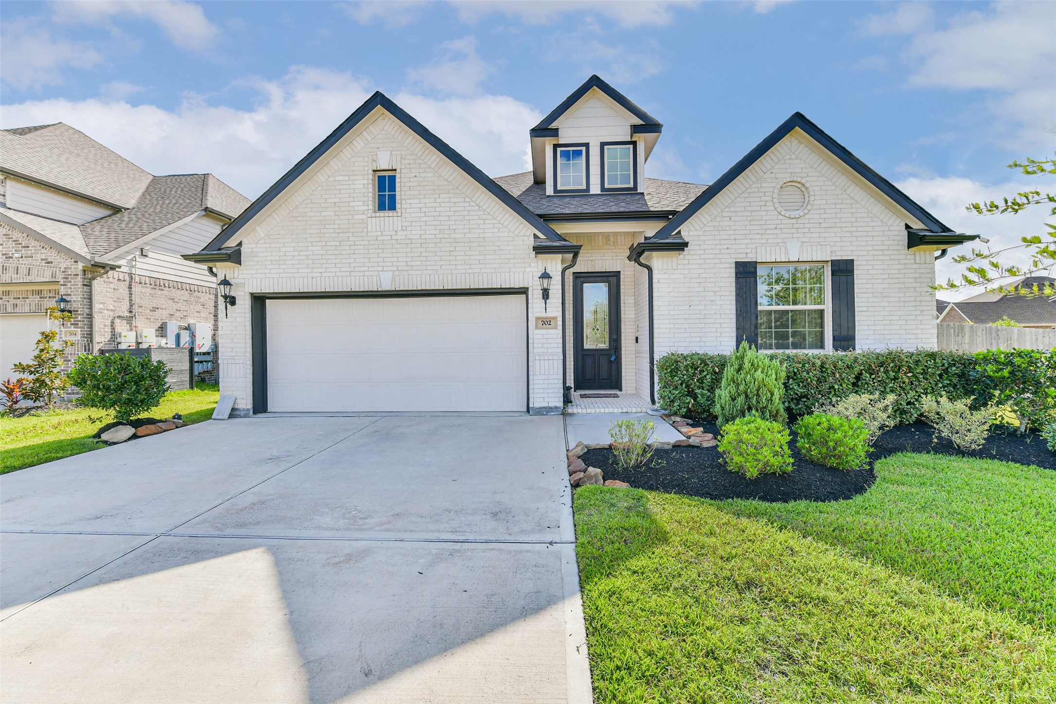 Charming white brick home with black accents, featuring a spacious two-car garage and well-maintained landscaping.