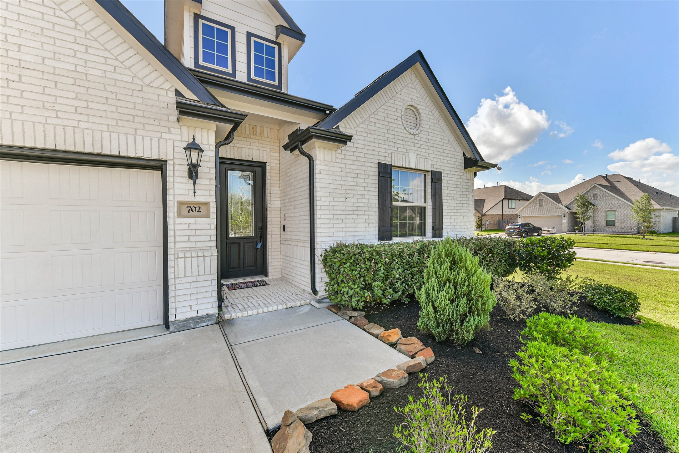 Charming brick home with a welcoming entrance, beautifully manicured landscaping, and a modern exterior featuring a stylish black door and window shutters.
