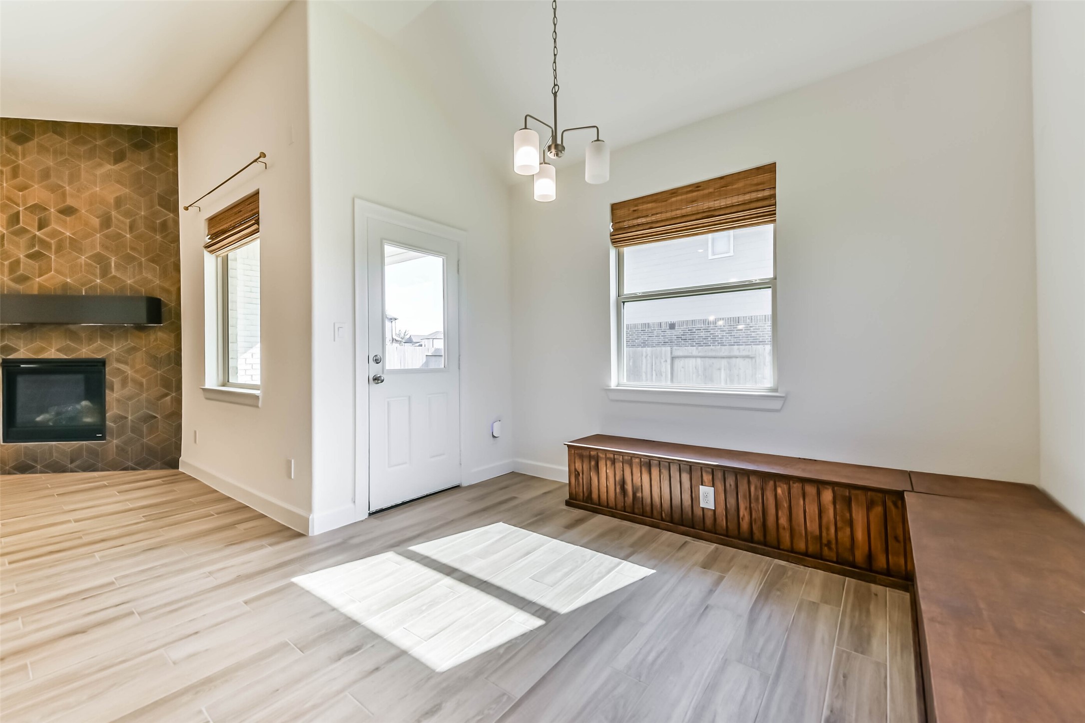 Bright and inviting living space featuring a stylish geometric accent wall with a cozy fireplace, elegant wooden bench seating, and abundant natural light.