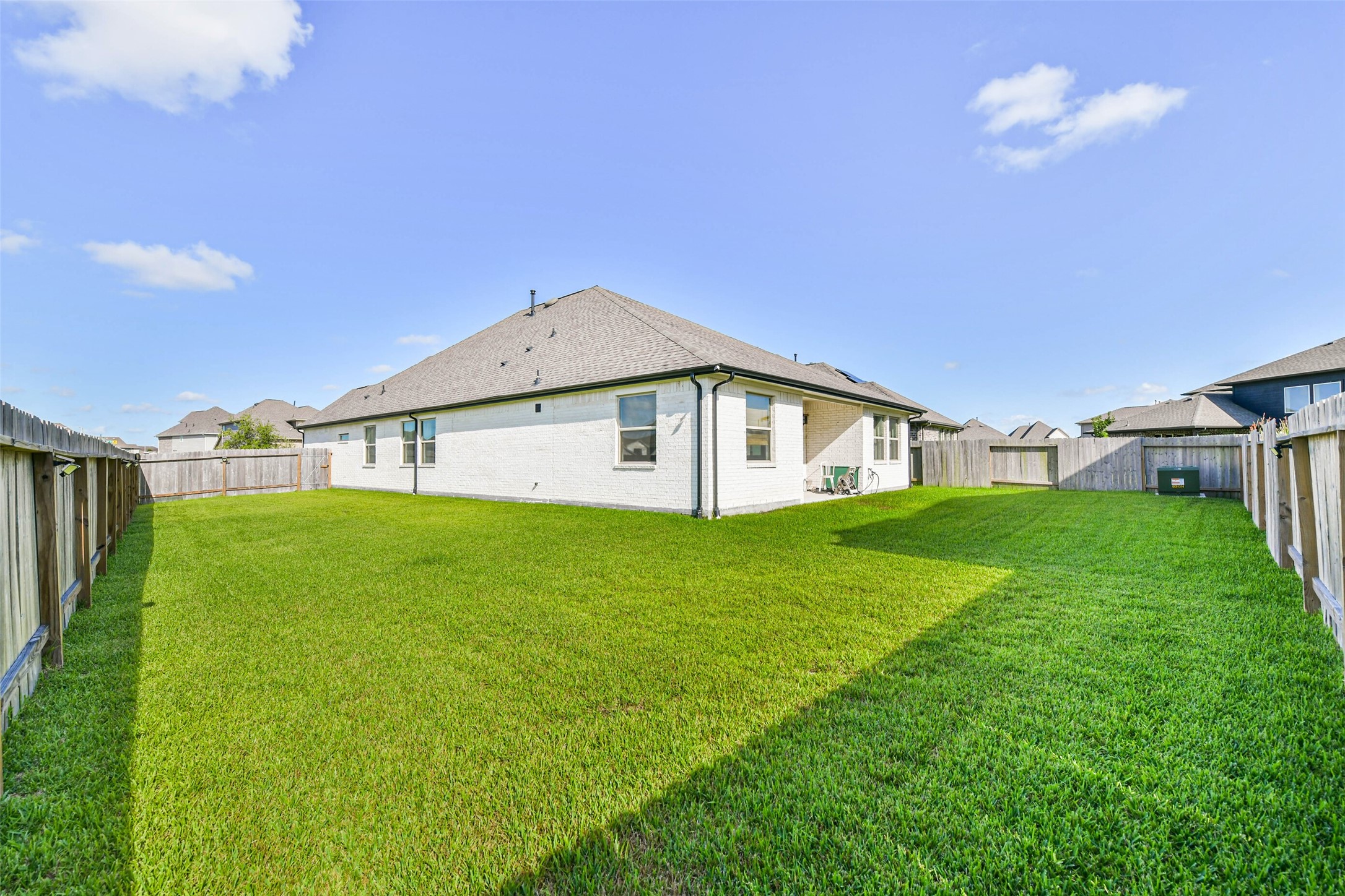 Spacious backyard with lush green lawn, perfect for outdoor activities, surrounded by a privacy fence and adjacent to a charming brick home.
