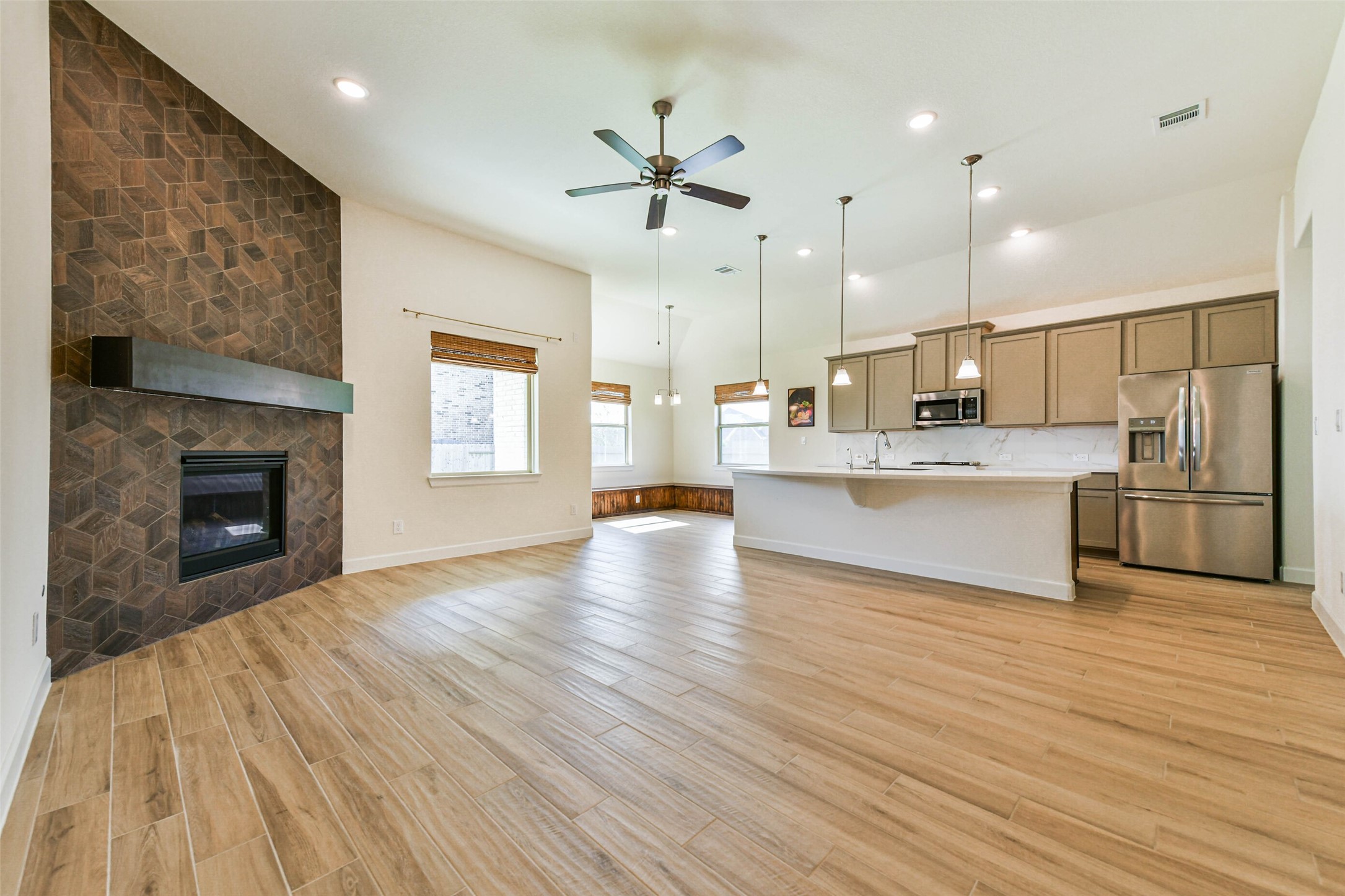 Spacious open-concept living area featuring a modern kitchen with stainless steel appliances, a cozy living room with a stylish tiled fireplace, and elegant wood flooring throughout.