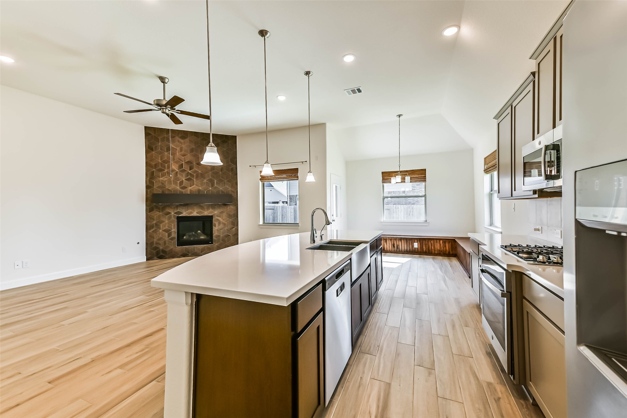 Bright and open kitchen and living area featuring a modern island with dual sinks, stylish cabinetry, and stainless steel appliances. A cozy fireplace with unique tile design enhances the spacious living room, while large windows bring in abundant natural light.