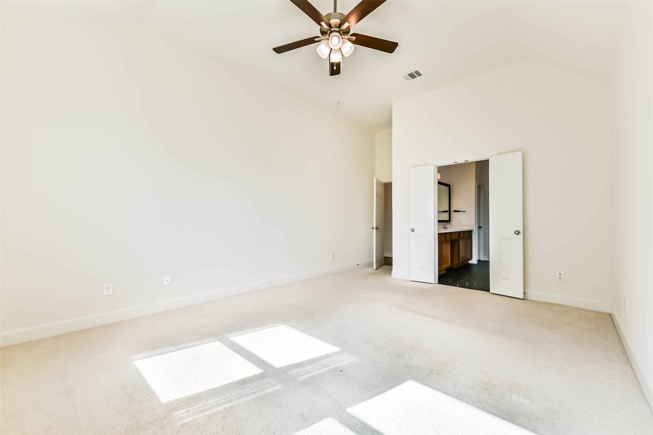 Another view of the primary bedroom with high ceilings, abundant natural light, and a ceiling fan, leading to an ensuite bathroom through double doors.