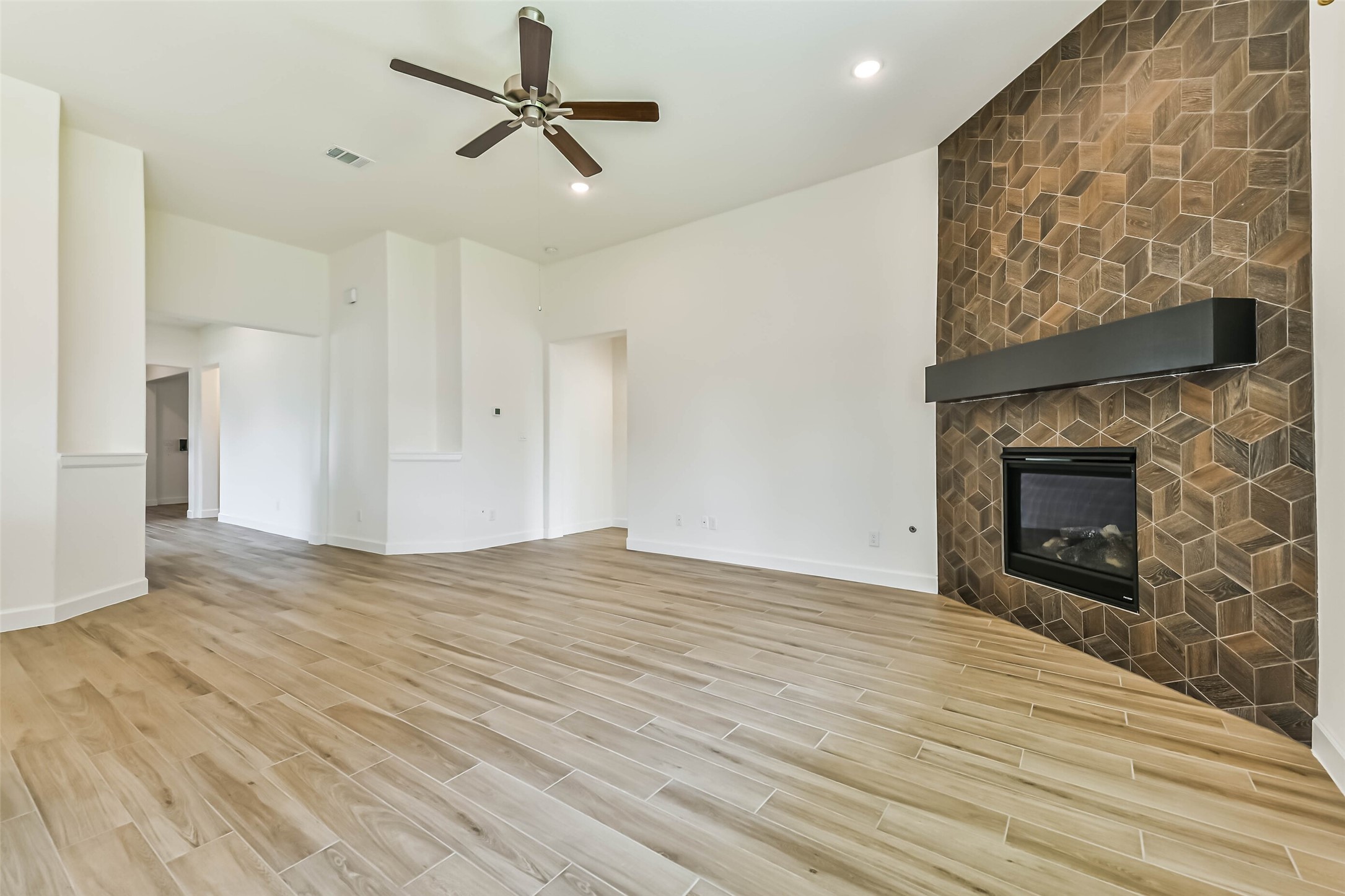 Spacious living area featuring elegant wood-look tile flooring and a striking geometric accent wall with a modern fireplace.