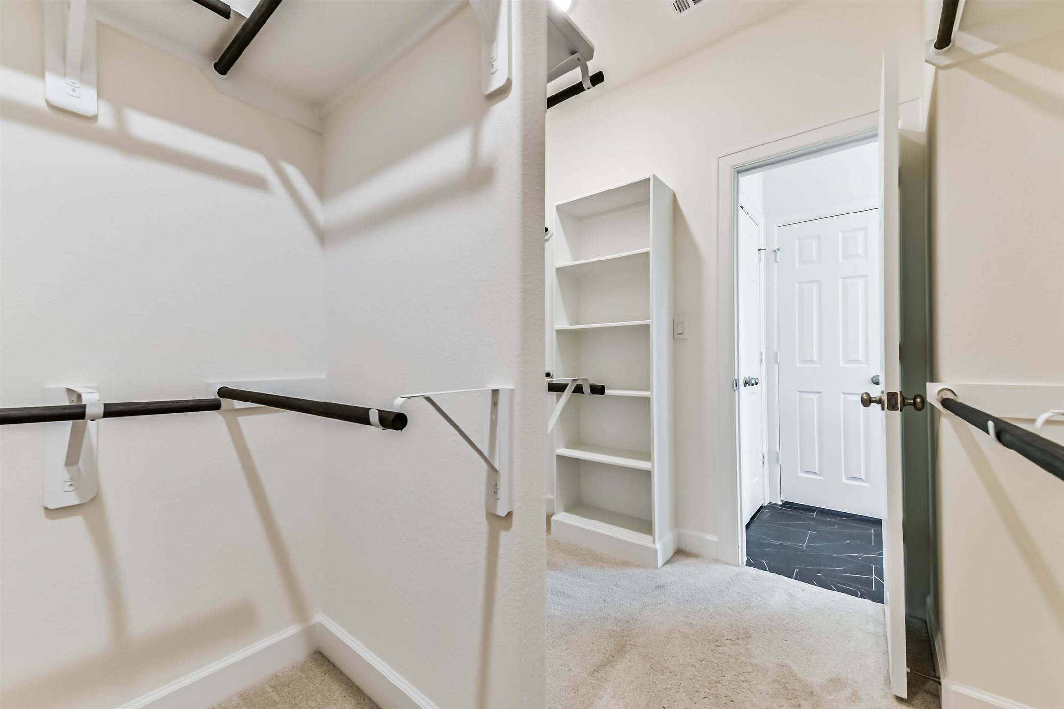 Spacious walk-in closet with ample shelving and hanging space, leading to a tiled hallway.