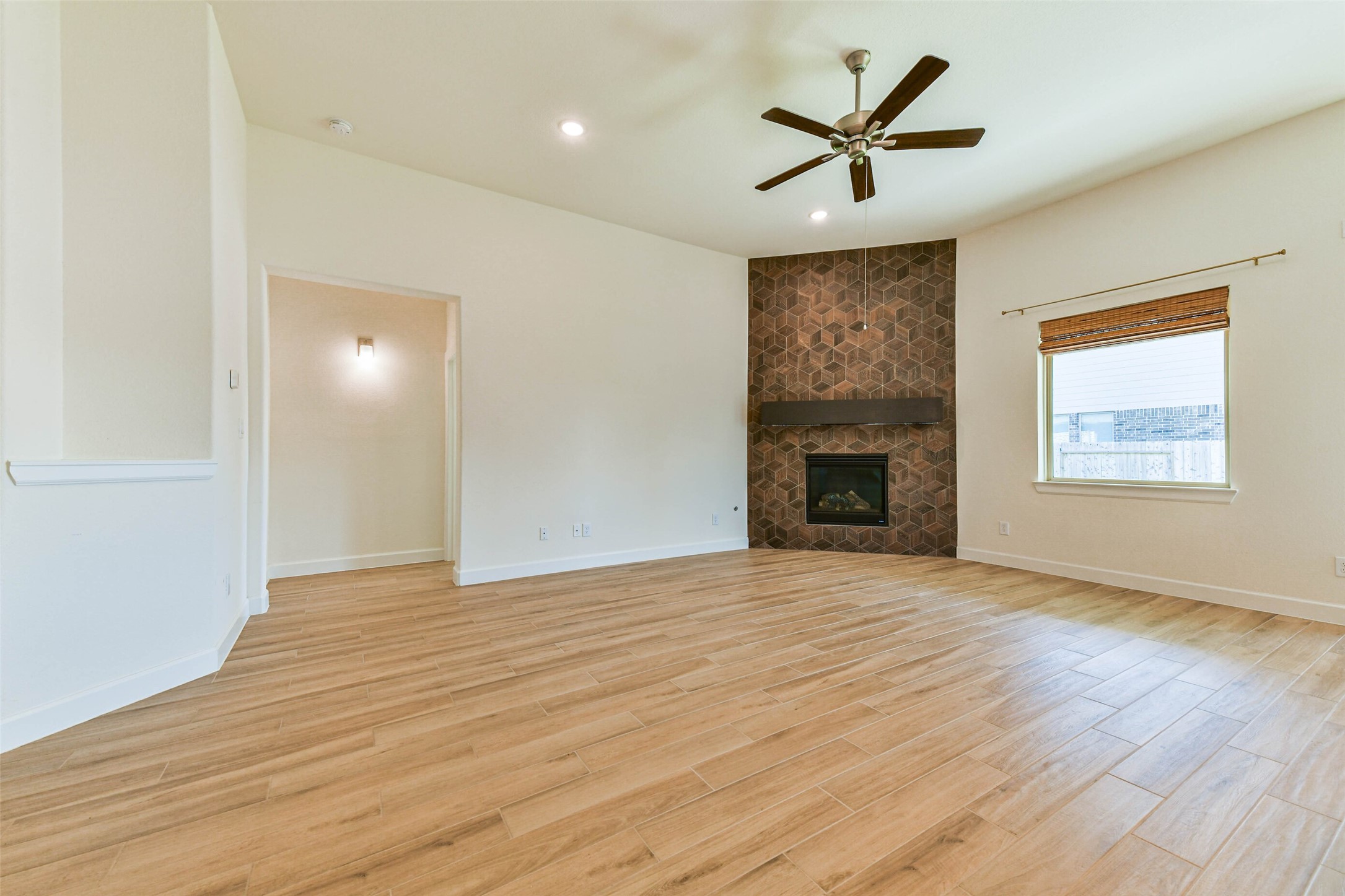 Spacious living room with a modern fireplace, elegant wood-style flooring, and ample natural light from a large window.