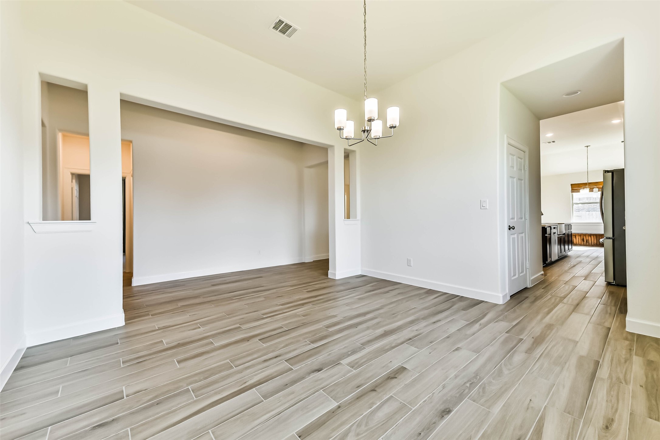 Spacious dining area with elegant wood-look tile flooring, modern chandelier, and open access to the kitchen, creating a seamless flow for entertaining.