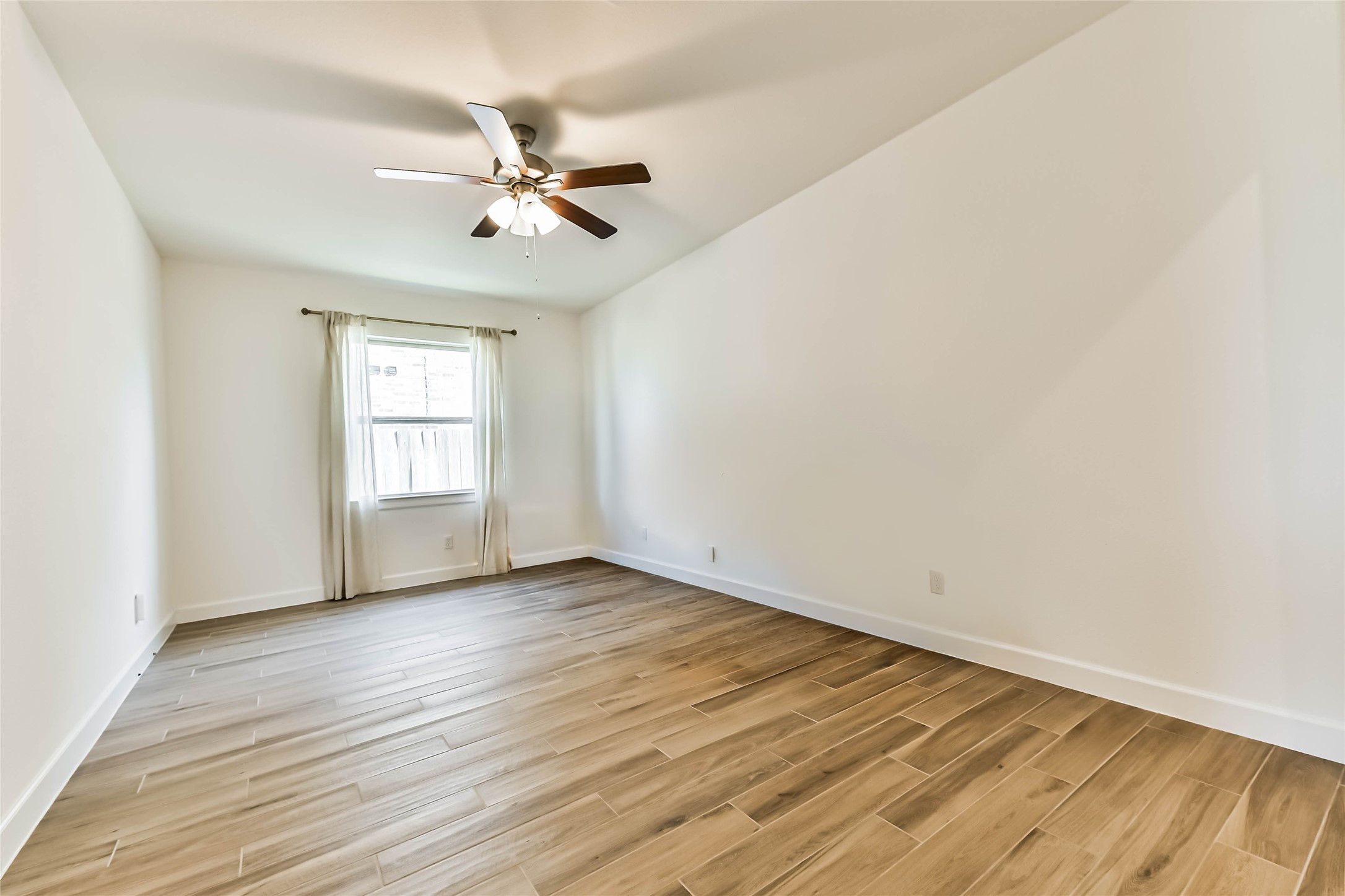 Spacious living area featuring elegant wood-look flooring, a modern ceiling fan, and bright, neutral walls that enhance natural light.