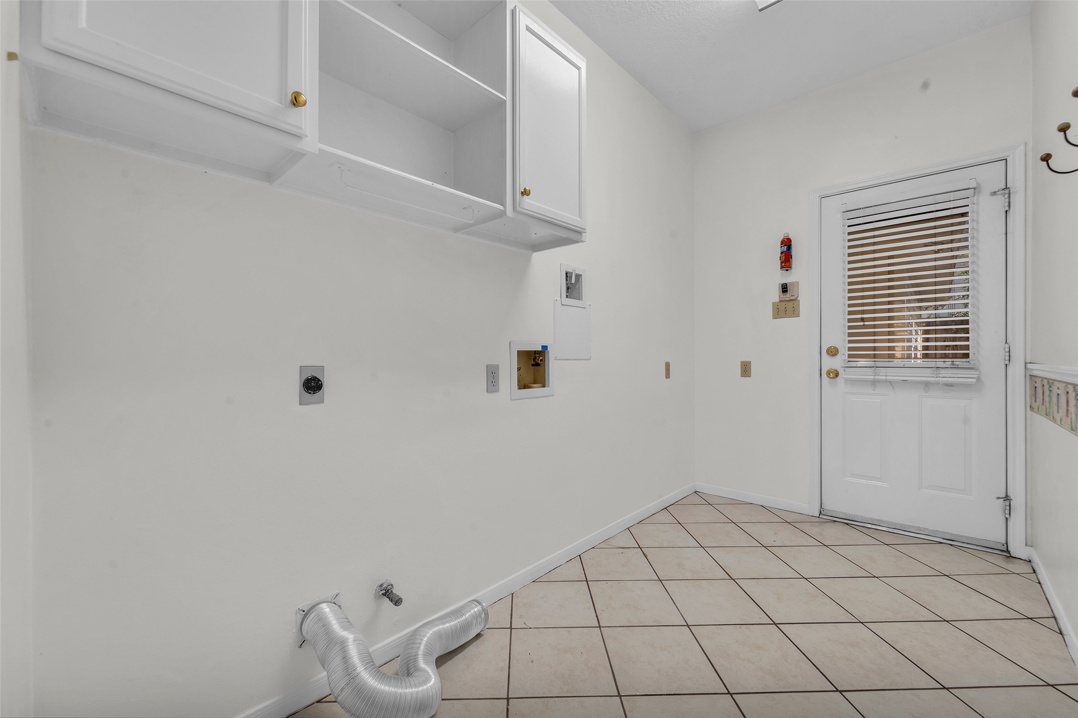 Spacious laundry room with tiled flooring, ample cabinet storage, and convenient outdoor access.