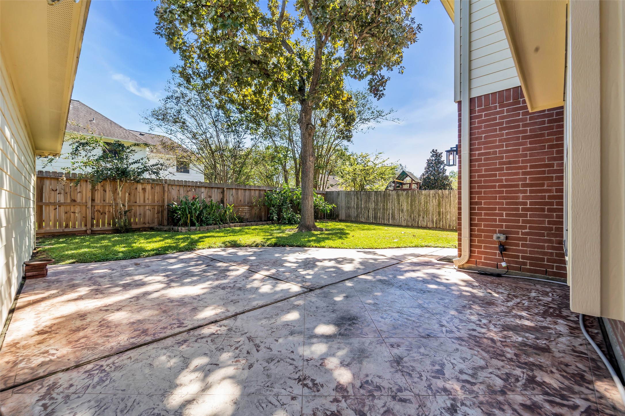 Charming backyard featuring a spacious patio with stamped concrete, ideal for outdoor gatherings, surrounded by lush greenery and mature trees for added privacy.