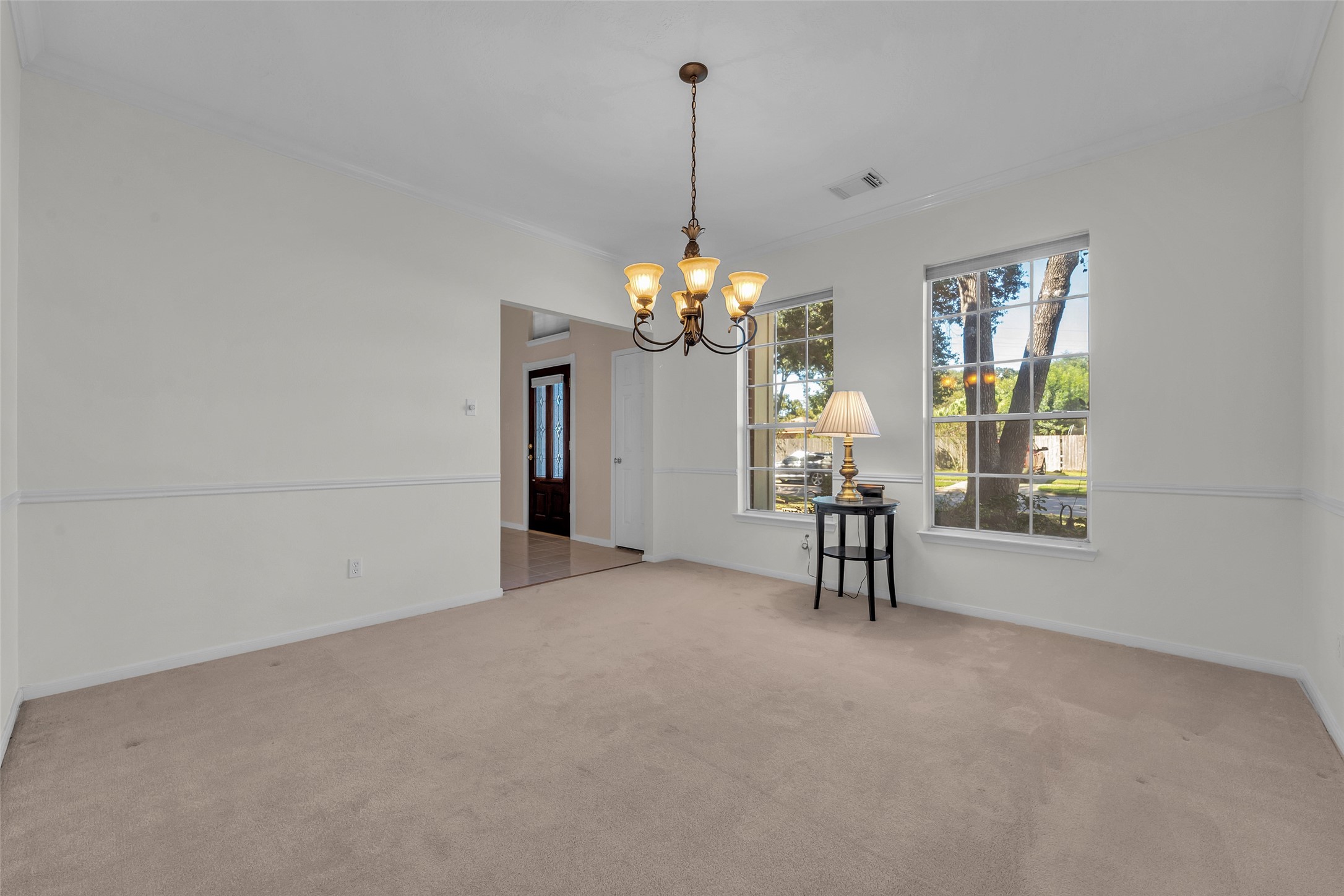 Bright dining area with a classic chandelier, neutral walls, and large windows offering a serene view of the garden.