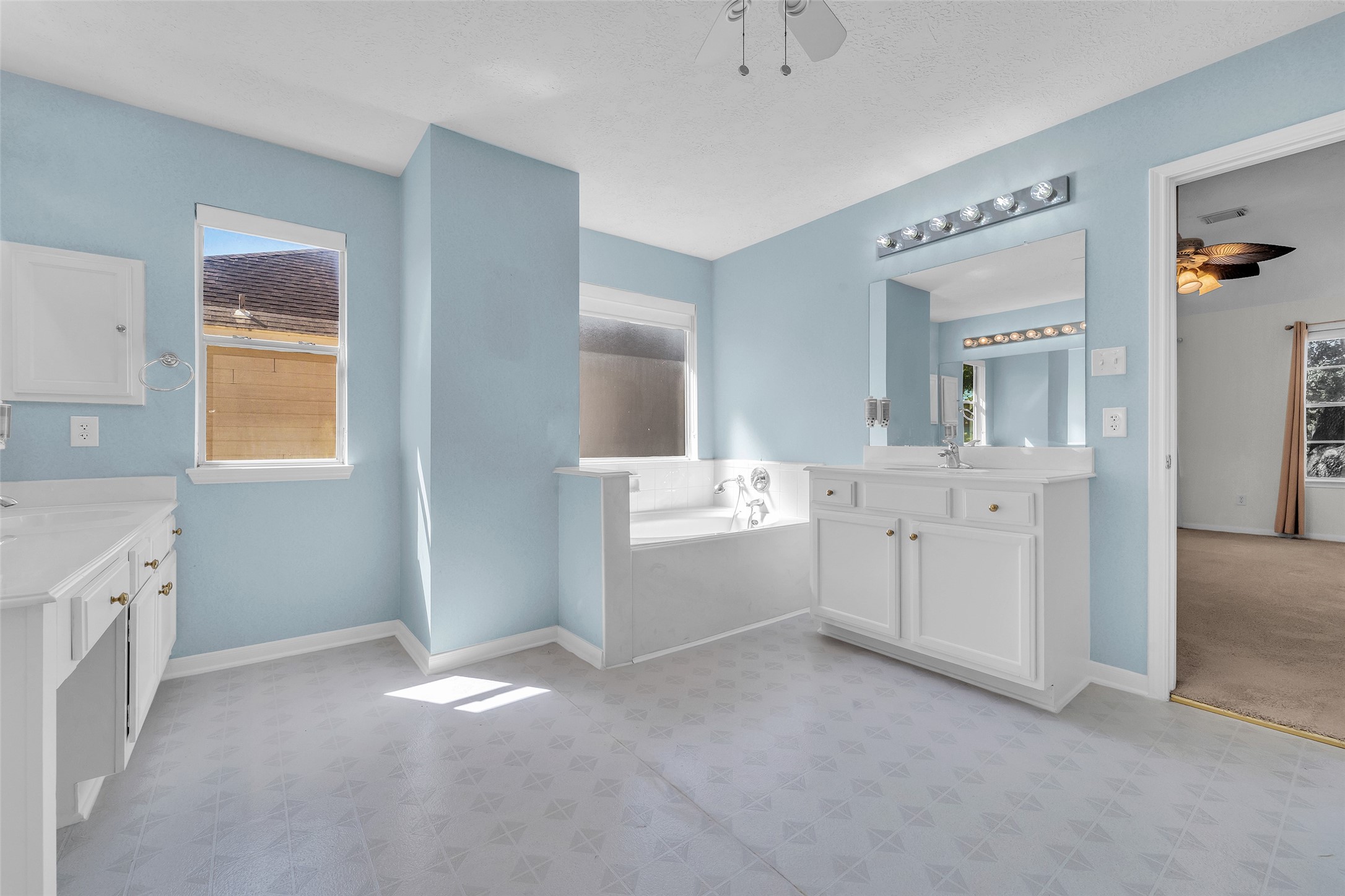 Spacious bathroom with soft blue walls, featuring a large vanity with ample storage, a luxurious soaking tub, and natural light streaming through the window.