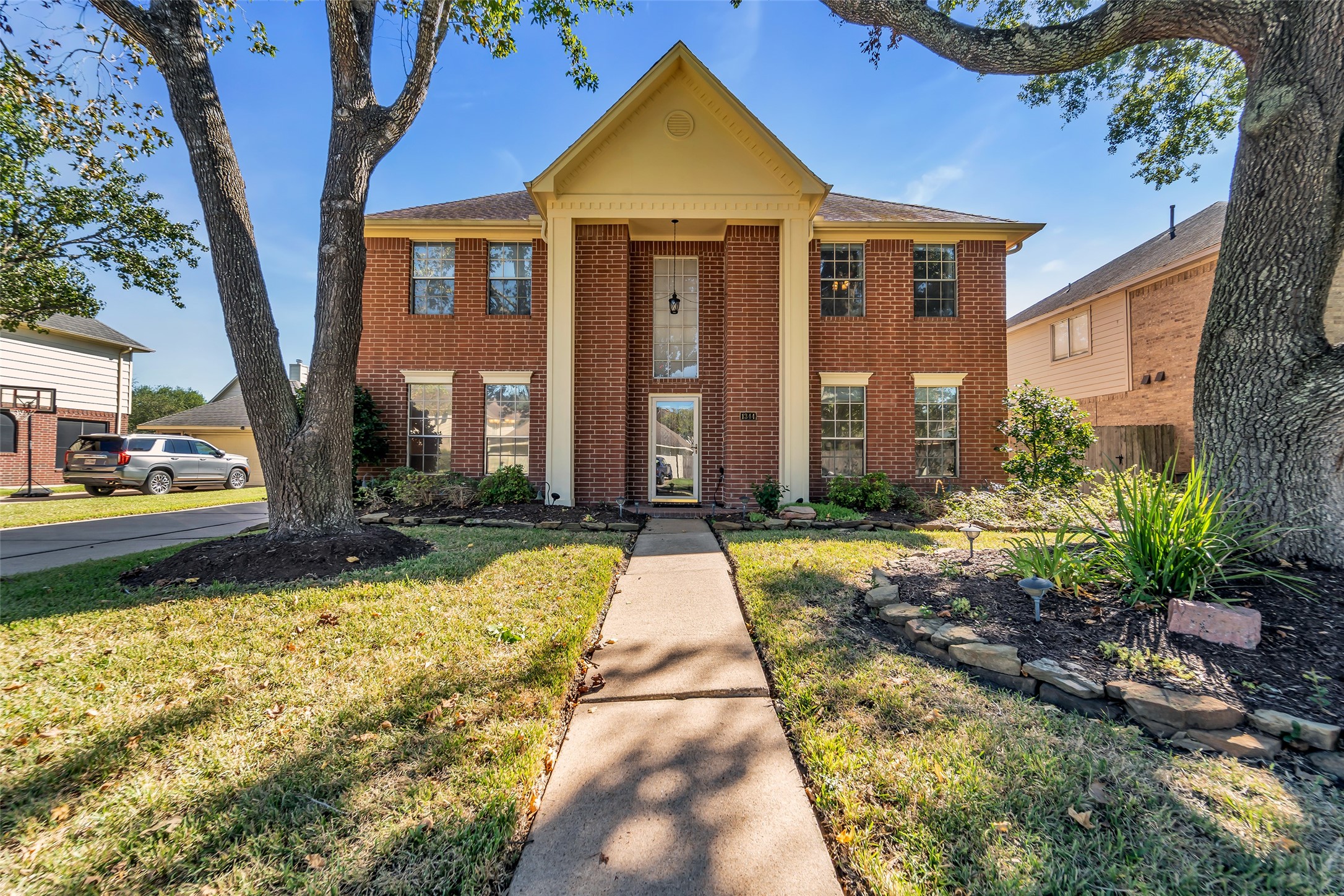 Stately brick home with a grand entrance, framed by mature trees and landscaped gardens, offering charming curb appeal.