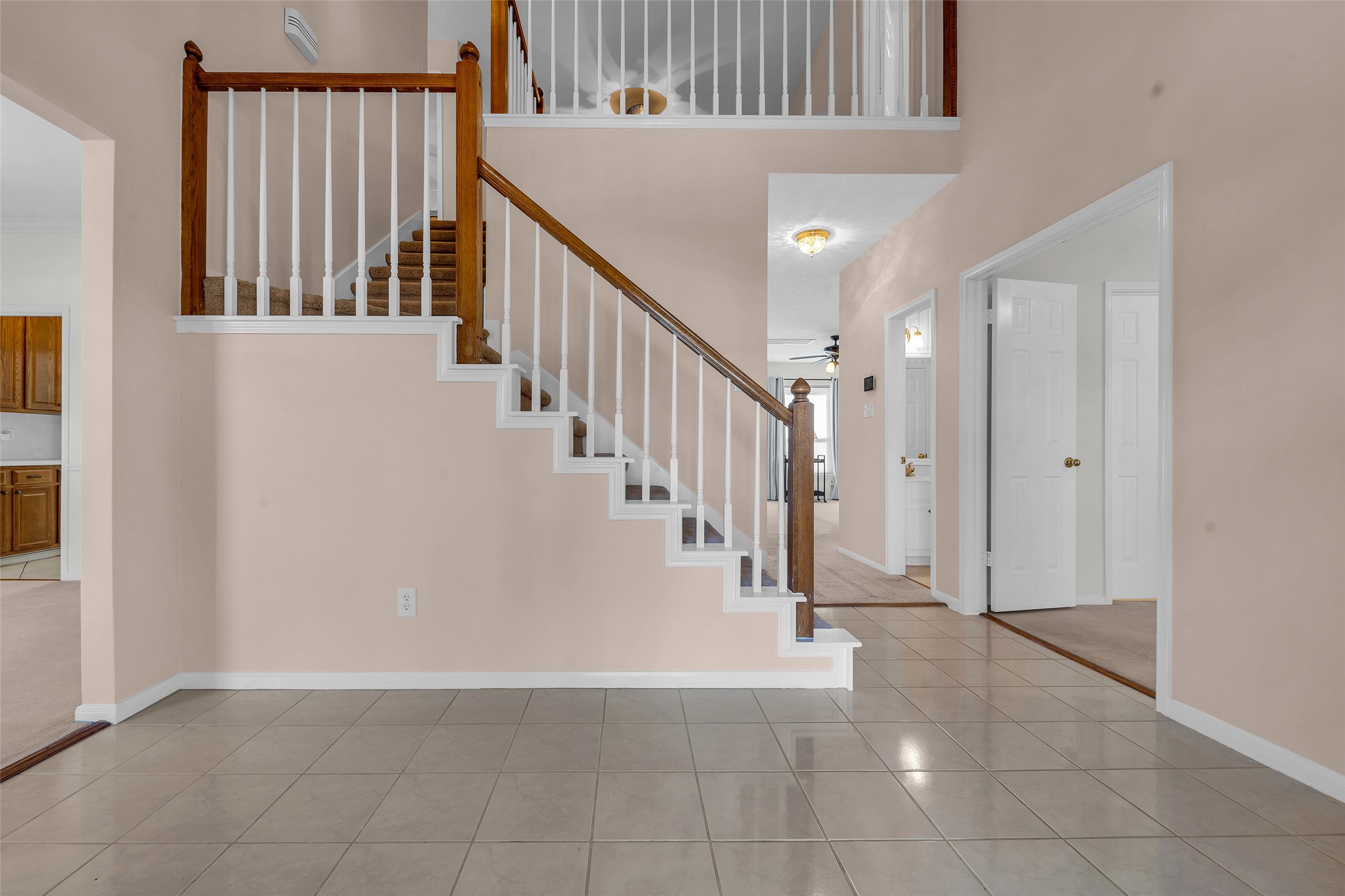 A welcoming foyer with tiled flooring leads to a staircase featuring elegant wooden railing, offering access to a spacious upper level. Adjacent rooms include a bright kitchen and cozy living area, perfect for family gatherings.