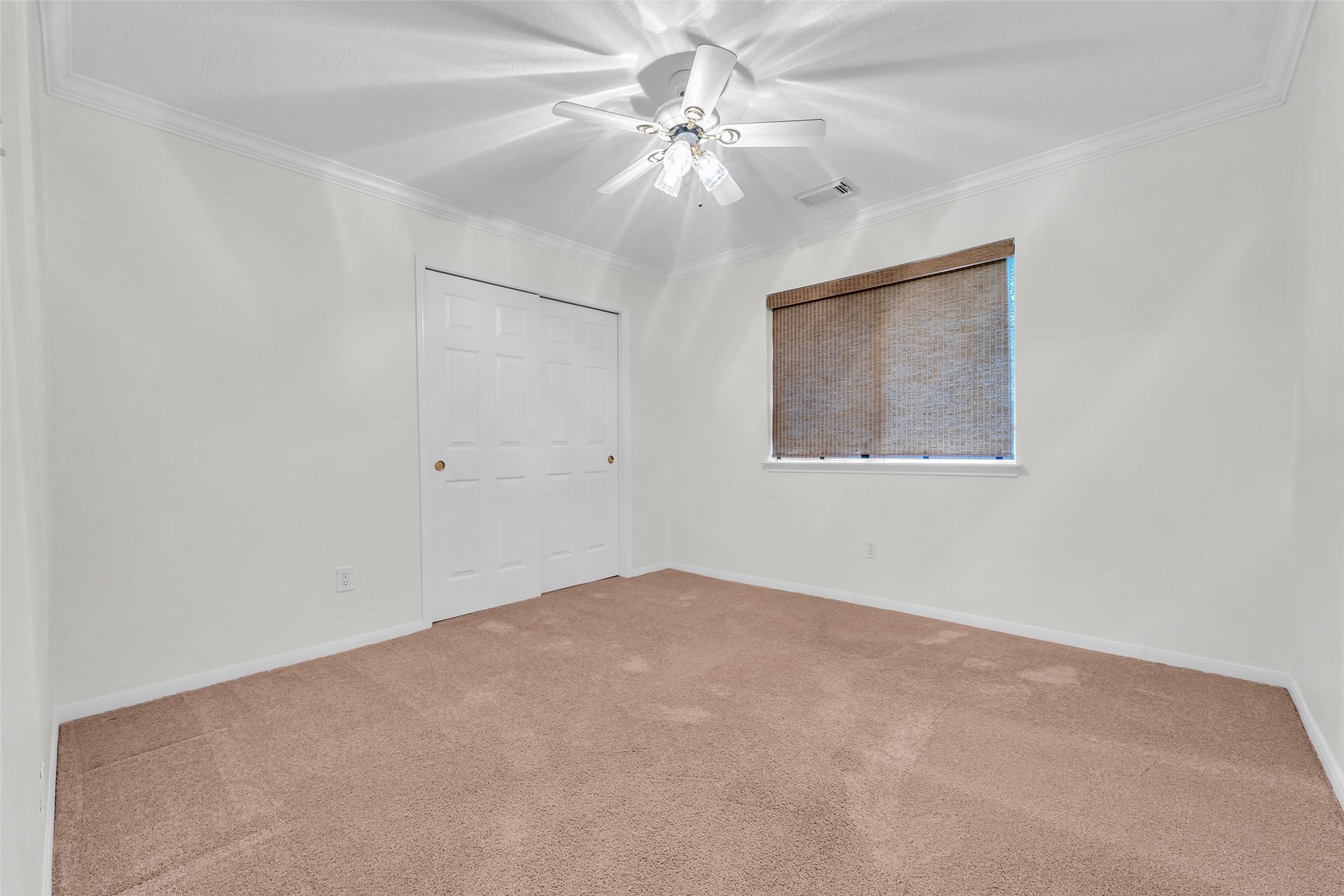 Spacious bedroom with plush carpeting, a ceiling fan, and ample closet space, enhanced by natural light from a cozy window with blinds.