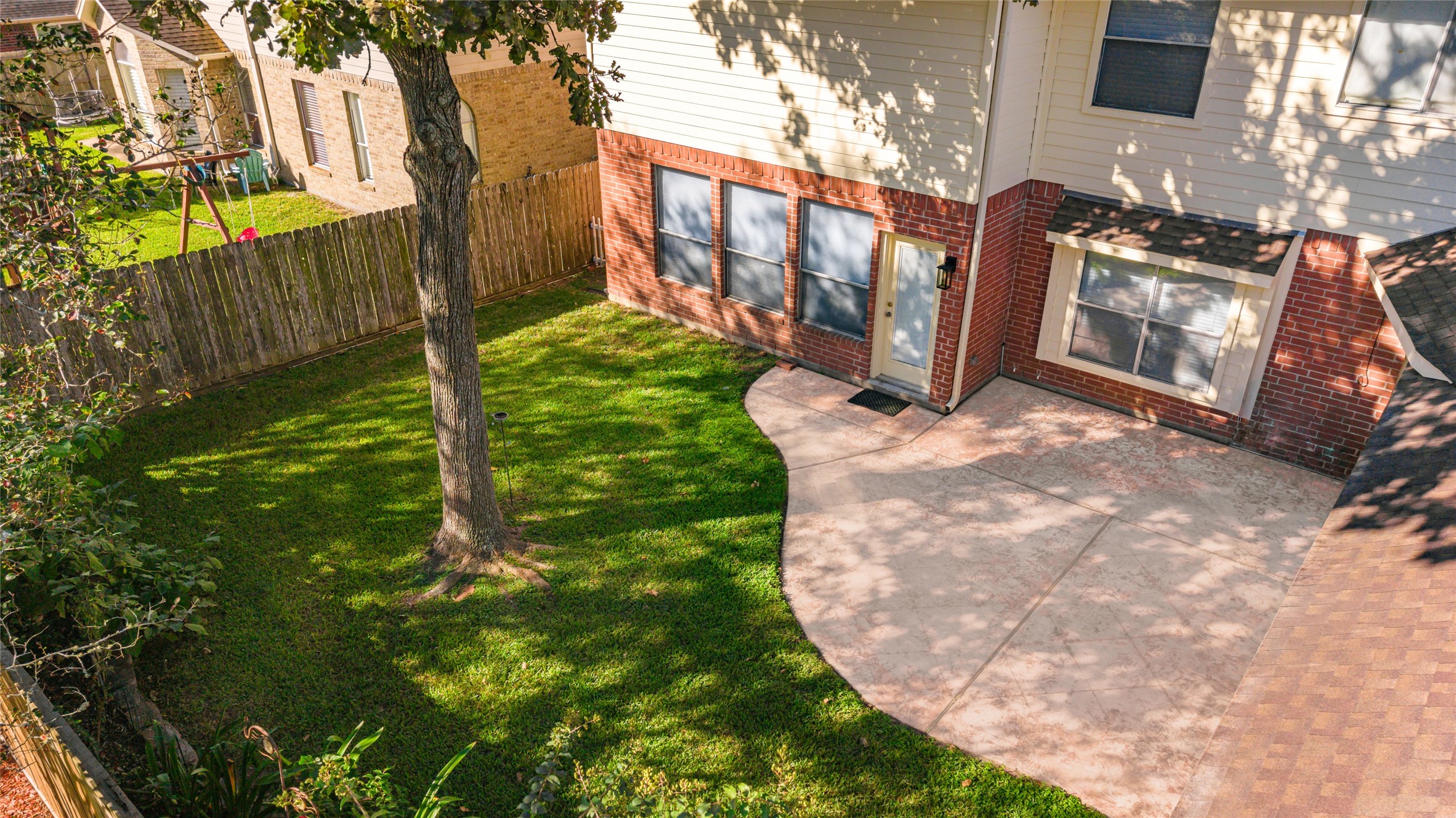 Charming backyard with a spacious patio perfect for entertaining, surrounded by lush greenery and a beautiful mature tree.