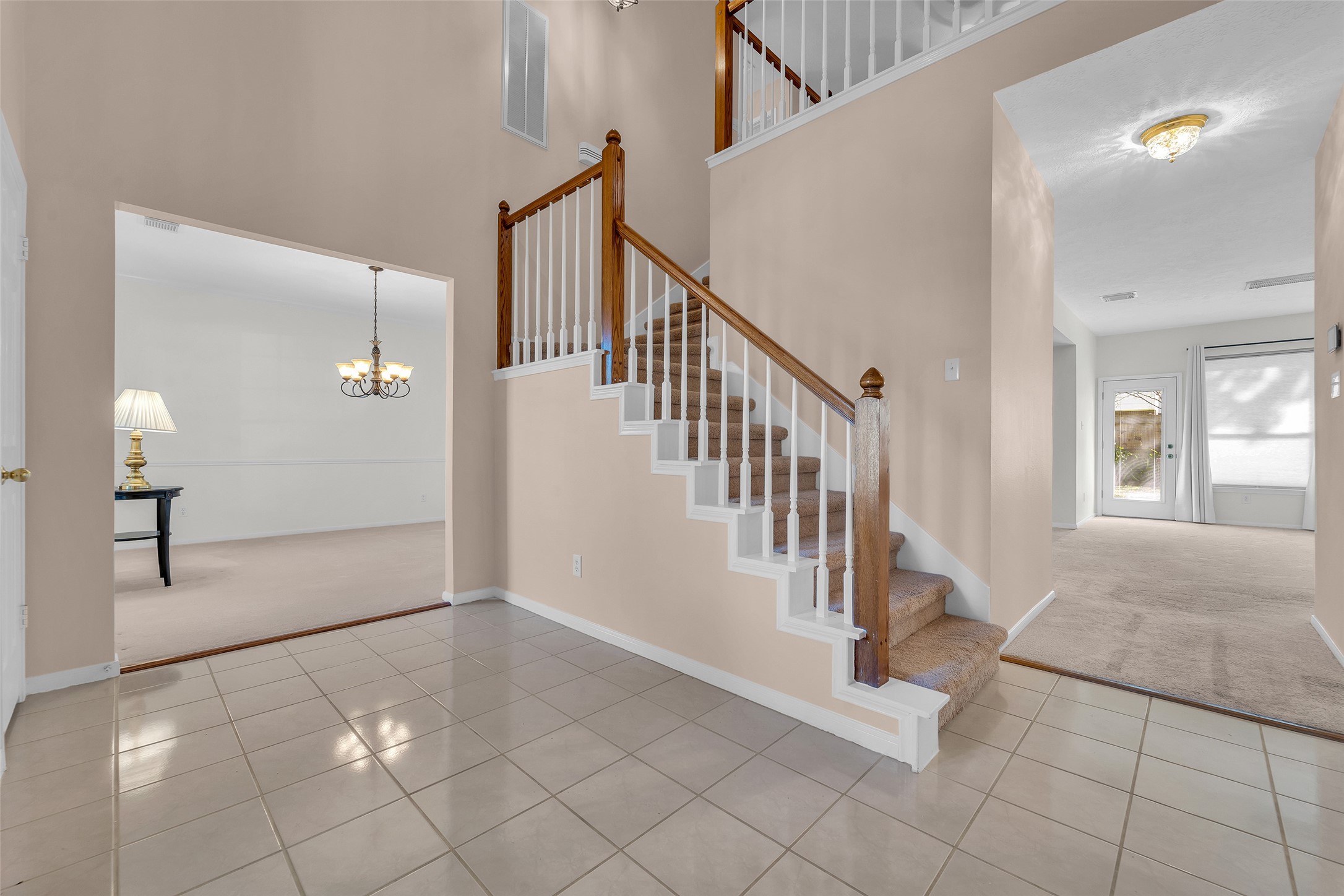 Spacious entryway features elegant tile flooring and a carpeted staircase with wooden accents, leading to well-lit living areas and a cozy dining room.