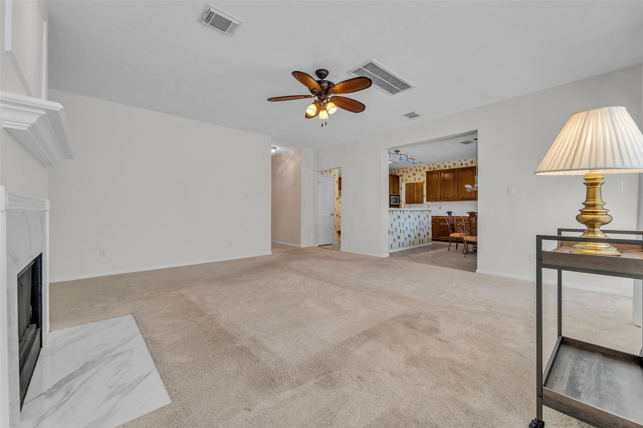 Spacious living area with a cozy fireplace, neutral carpeting, and direct access to the kitchen, perfect for entertaining.