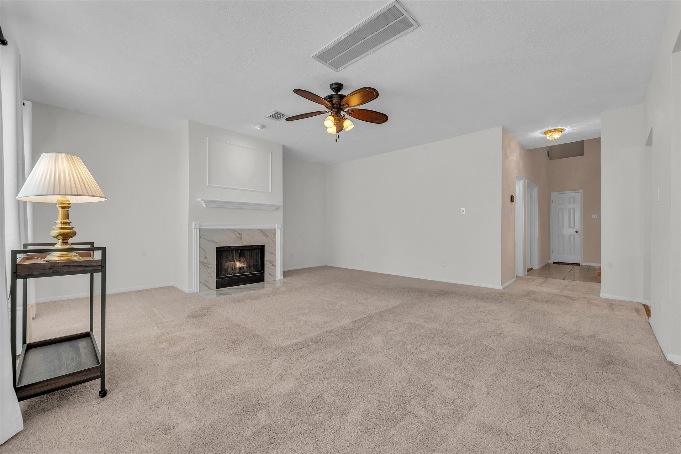 Spacious living room features a cozy fireplace, neutral carpeting, and a ceiling fan, offering a warm and inviting atmosphere.