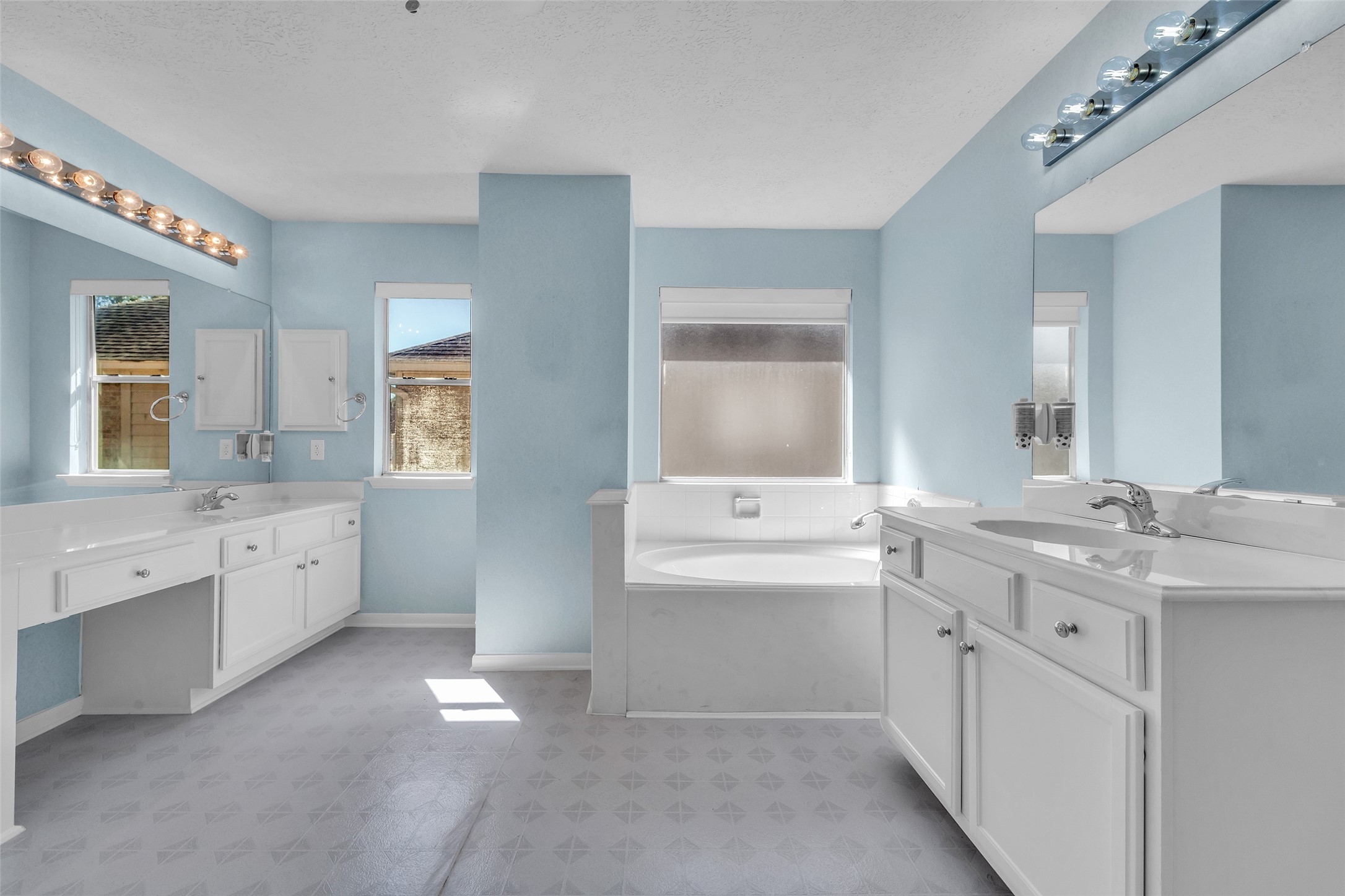 Spacious bathroom featuring dual vanities, a large soaking tub, and ample natural light, all set against soothing blue walls.
