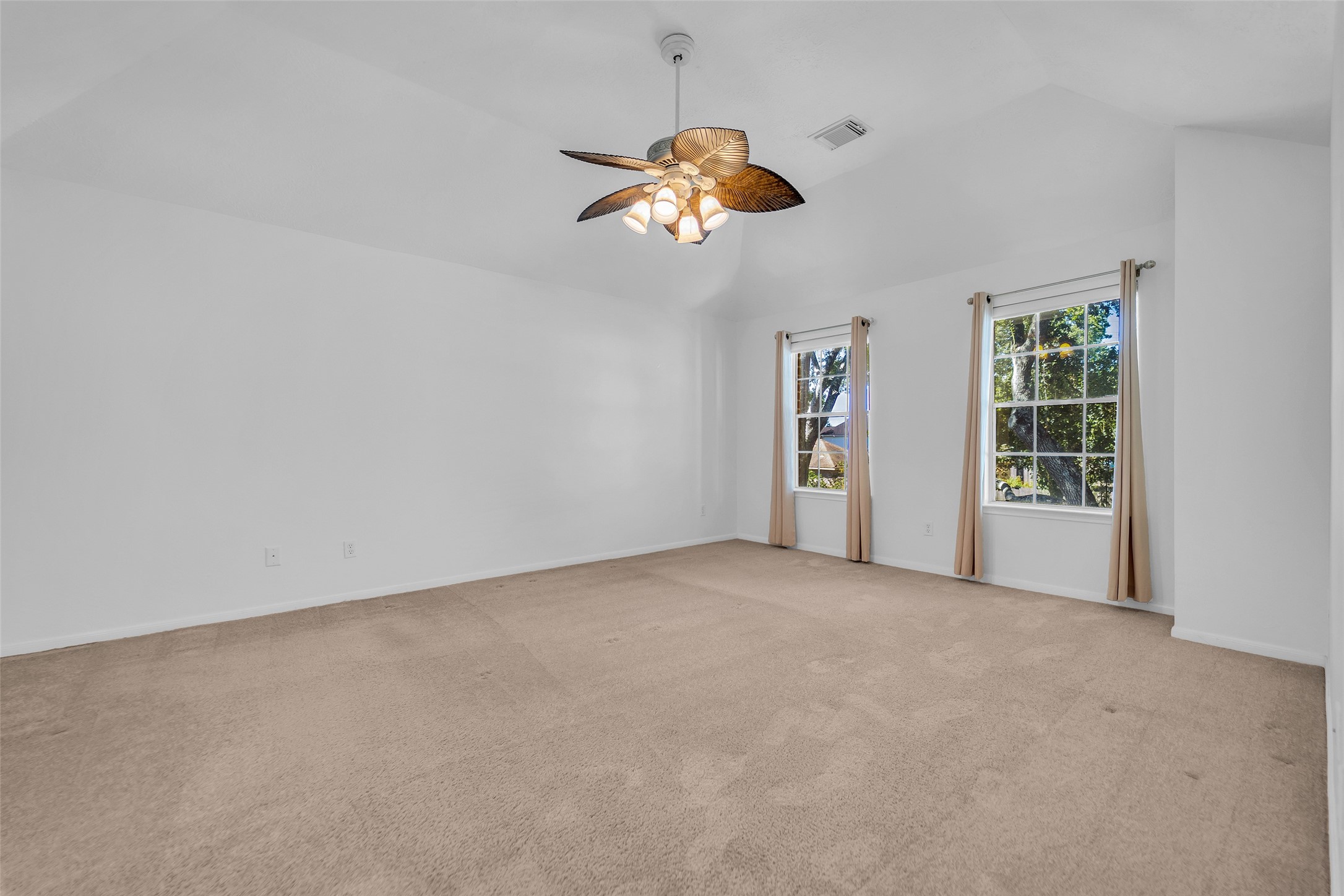 Spacious bedroom with neutral carpet, large windows for natural light, and a stylish ceiling fan.
