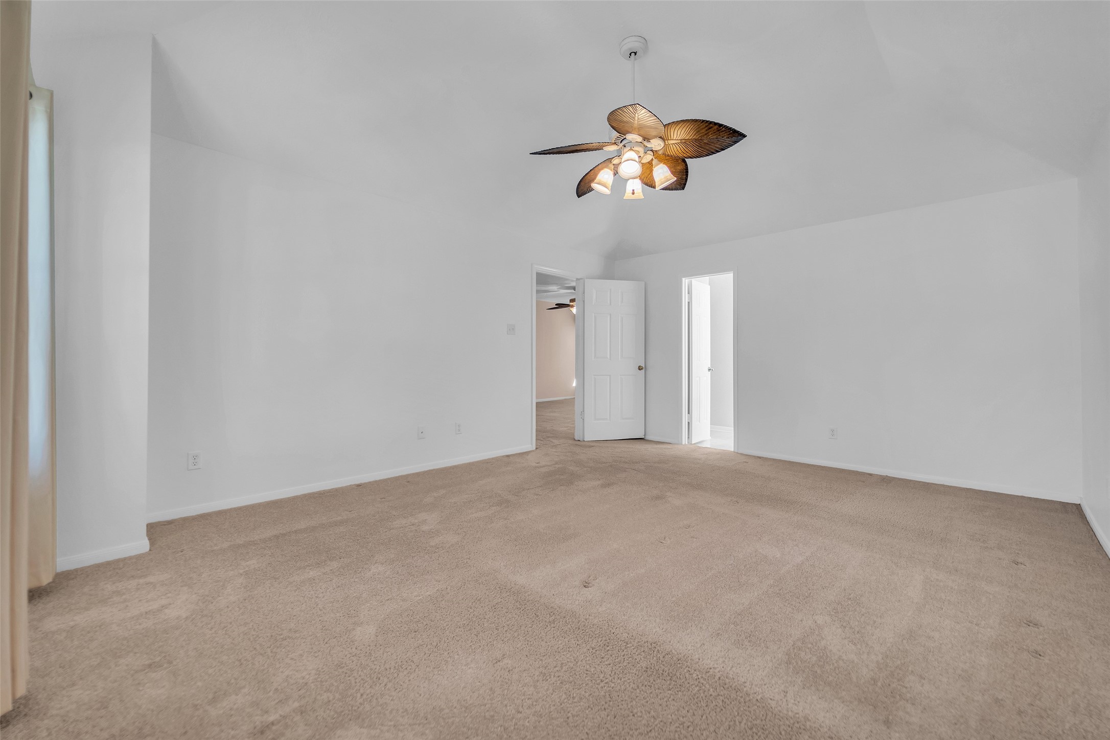 Spacious bedroom with a vaulted ceiling, featuring a unique ceiling fan and neutral-toned carpet, offering ample natural light and a cozy atmosphere.