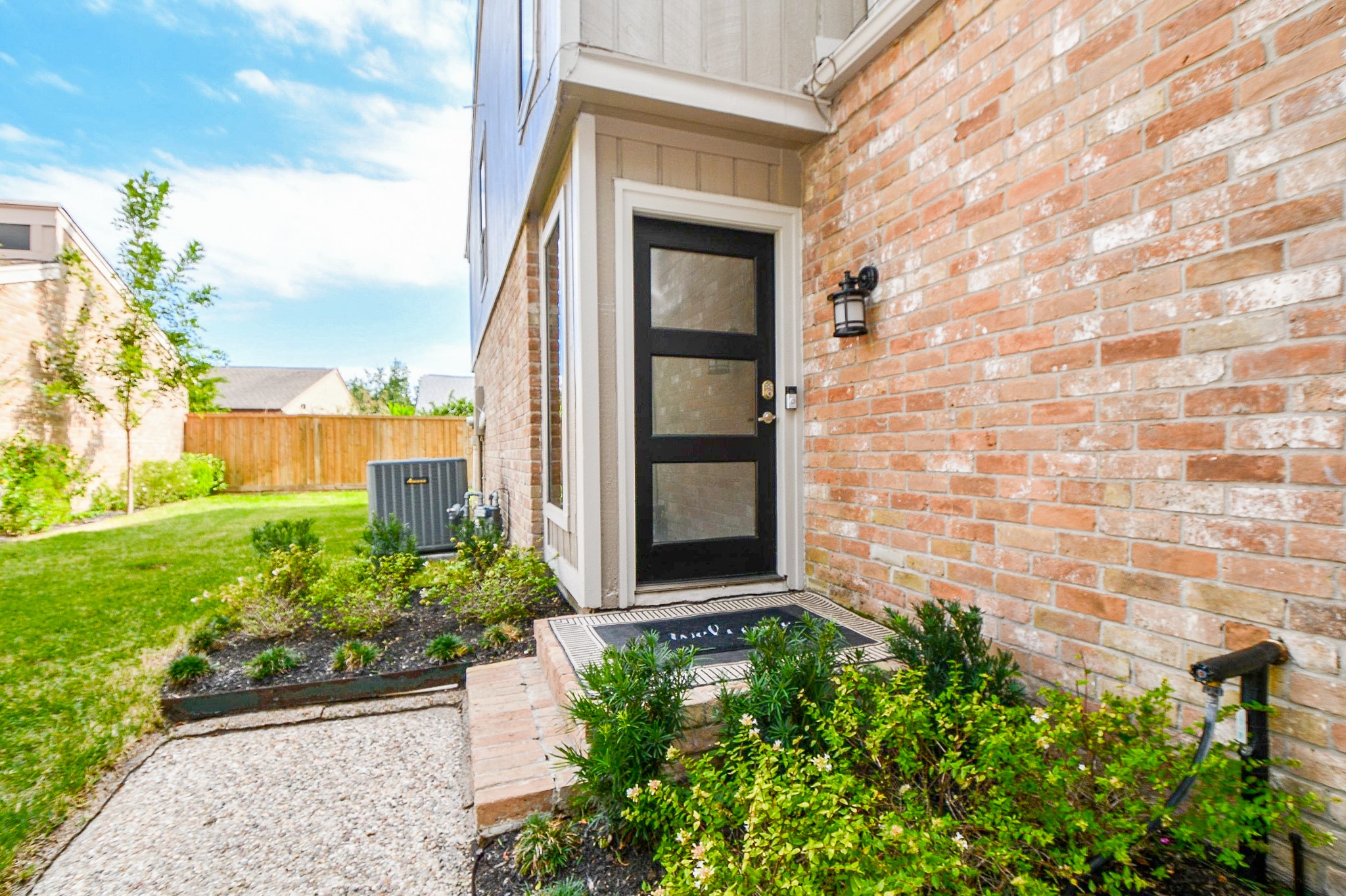 A modern side entry with a glass-panel door, set among fresh landscaping.
