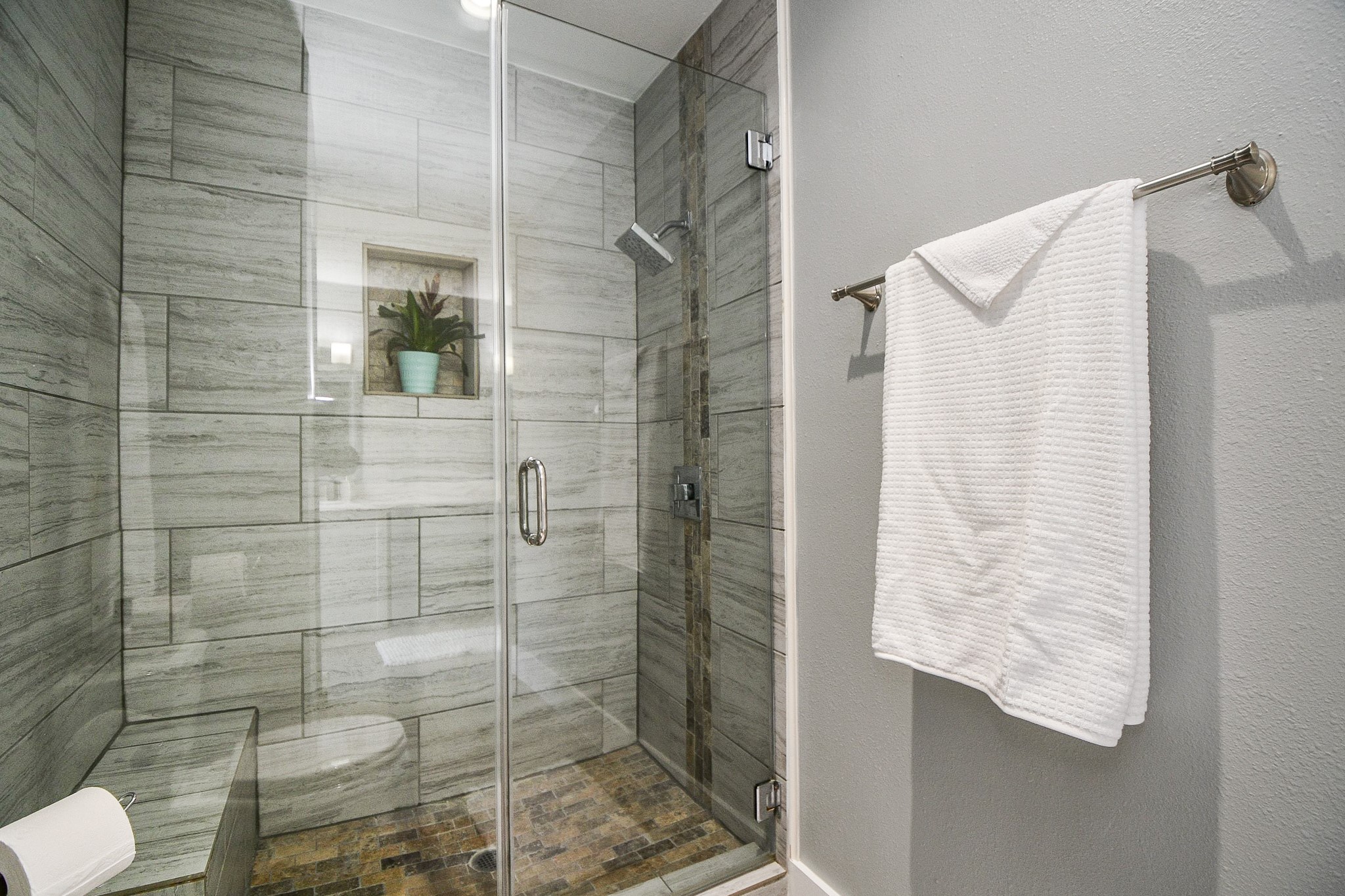 The frameless glass walk-in shower has large-format tile, a built-in niche, and a bench.