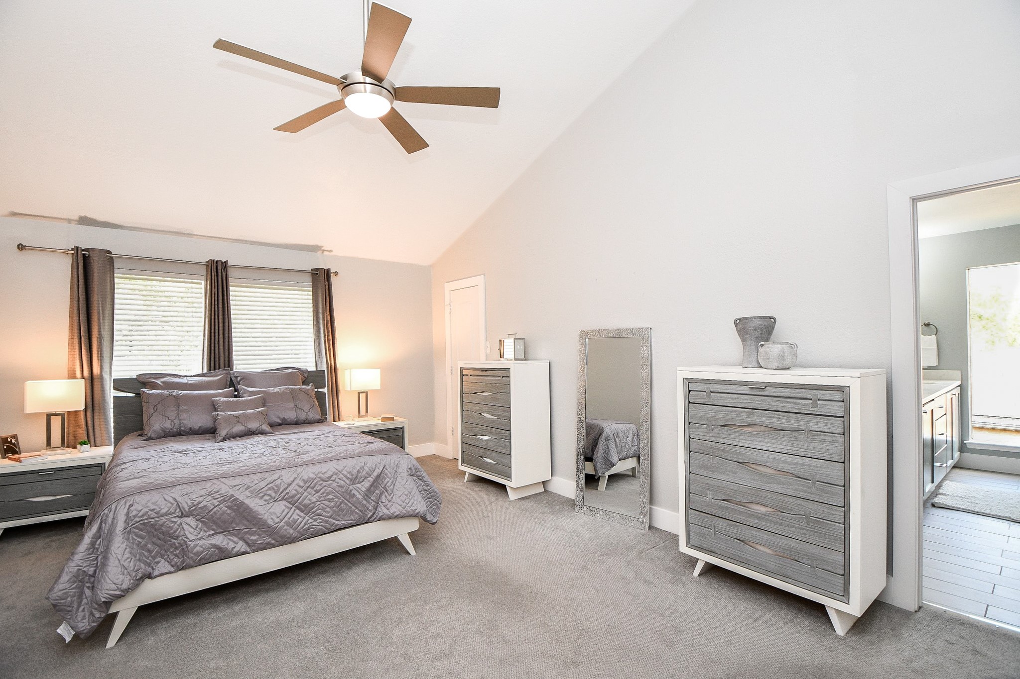 The spacious primary bedroom has vaulted ceilings, a ceiling fan, and plush carpet.