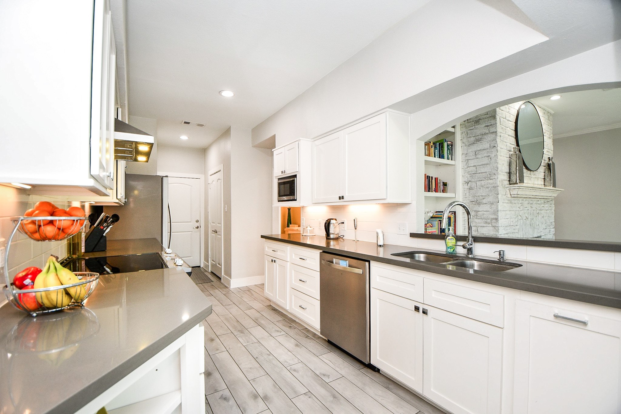 A deep stainless sink with a gooseneck faucet sits beside a pass-through window with built-in shelving.