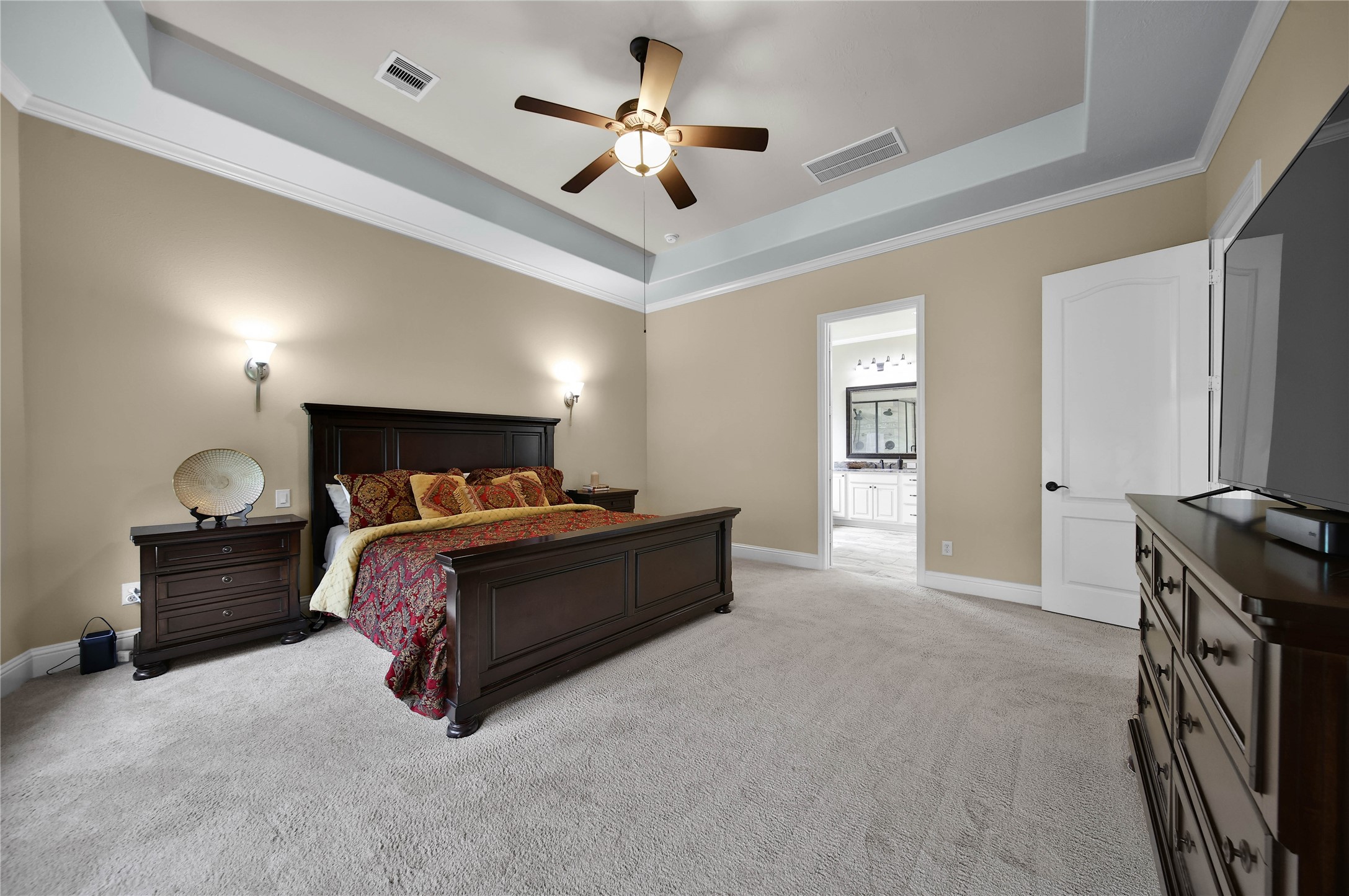 The primary suite features a beautiful tray ceiling with elegant lighting sconces and opens to a luxurious bath, creating a relaxing retreat to unwind at the end of the day.