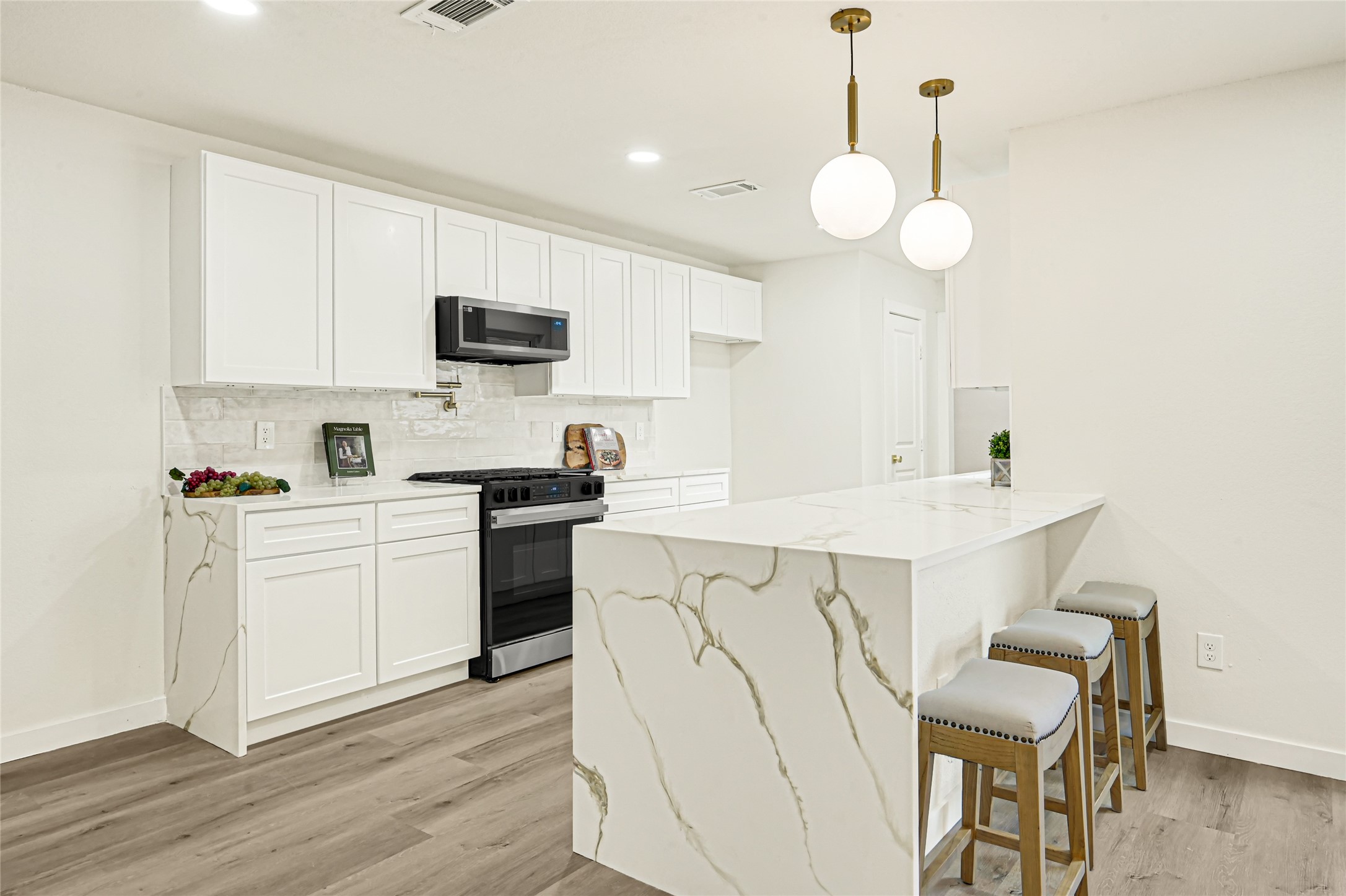 Beautifully remodeled kitchen featuring quartz countertops with waterfall-style island, white shaker cabinetry, stylish brushed gold accents, and modern pendant lighting. Perfect for cooking and entertaining!
