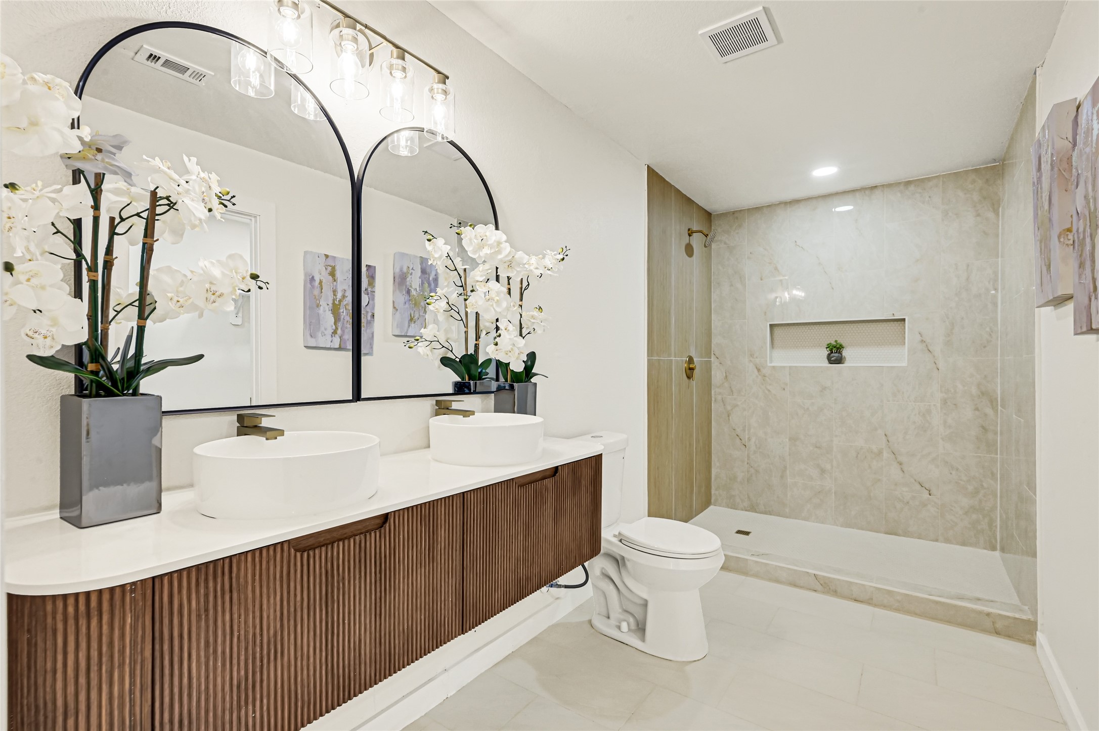 Spa-inspired primary bathroom featuring dual vanities, elegant brushed gold fixtures, and a beautifully tiled walk-in shower