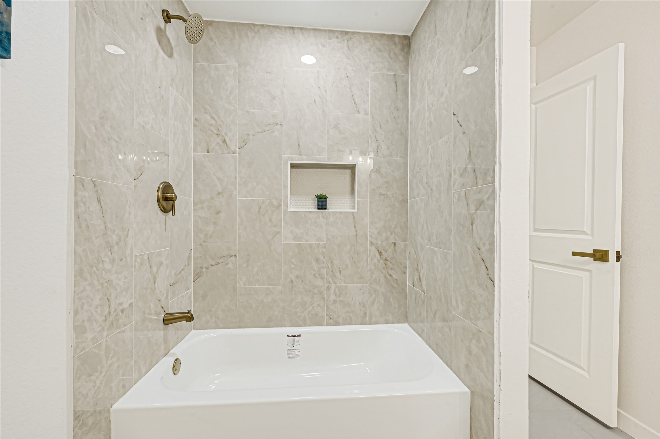 Updated guest bathroom featuring a beautifully tiled tub and shower with elegant brushed gold fixtures.