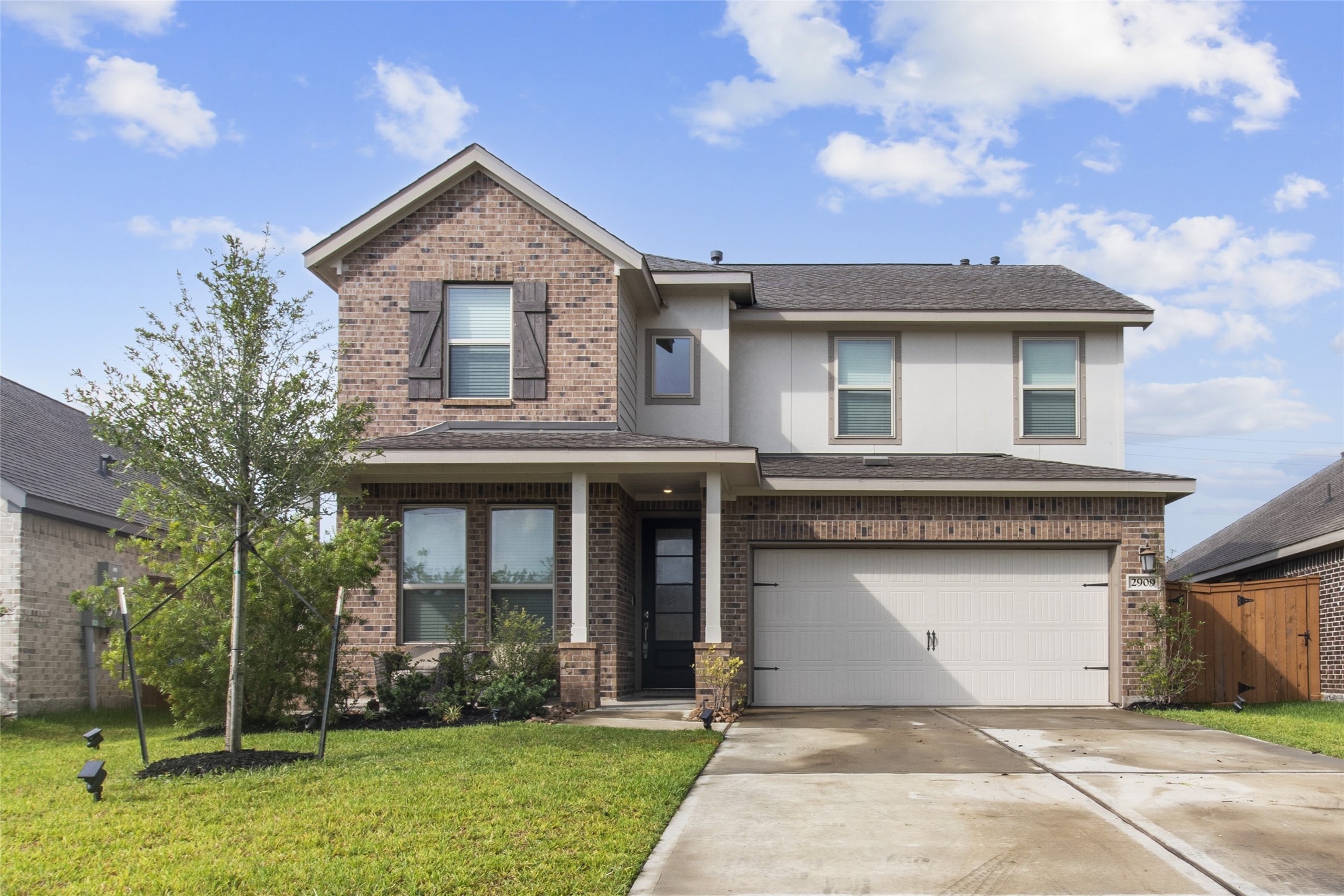 Charming two-story home with a classic brick faade, featuring a spacious two-car garage and a welcoming front porch. Lush landscaping enhances its curb appeal.