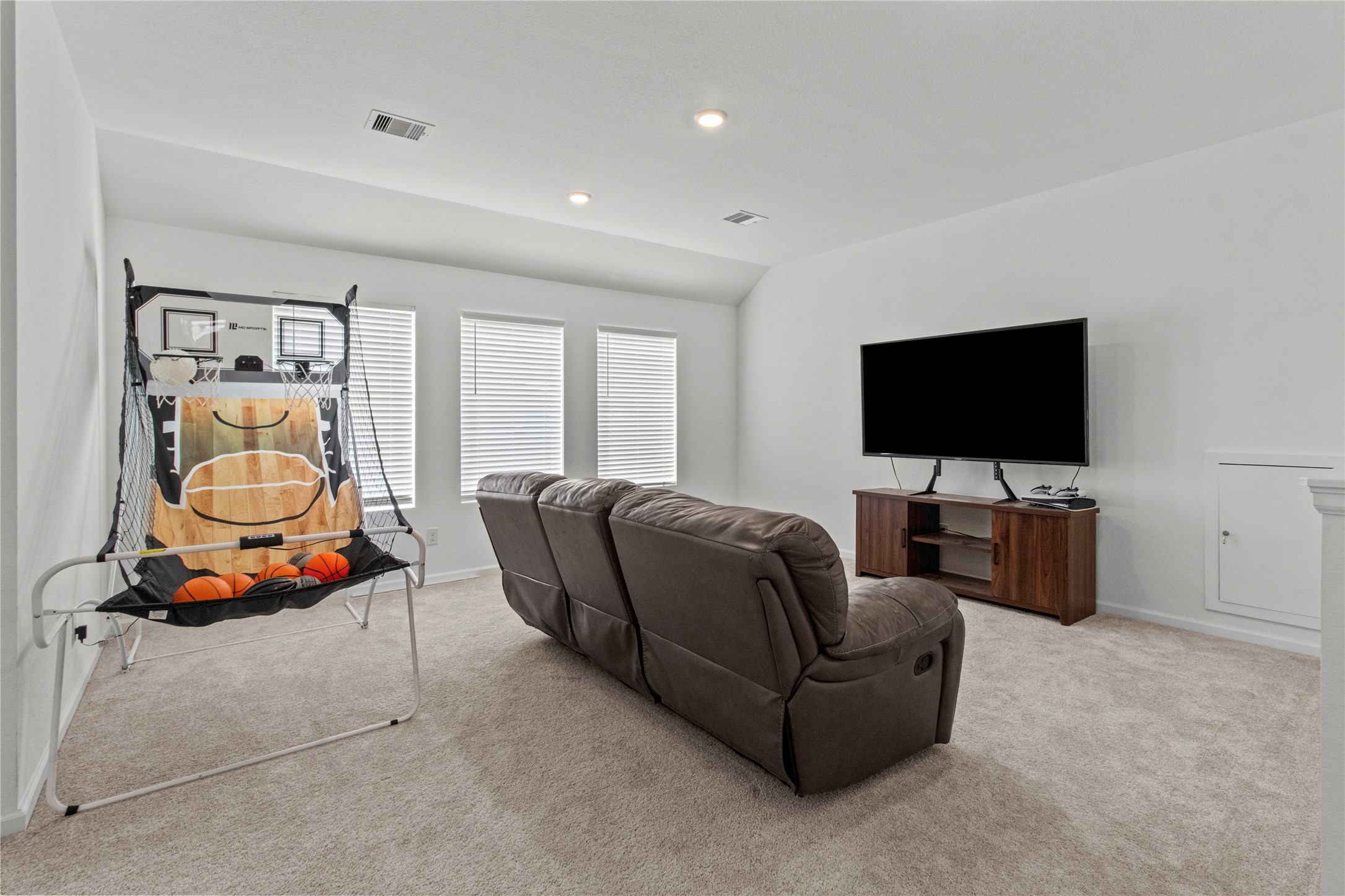 Spacious entertainment room featuring comfortable seating, a large TV, and an indoor basketball game, perfect for family fun and relaxation.