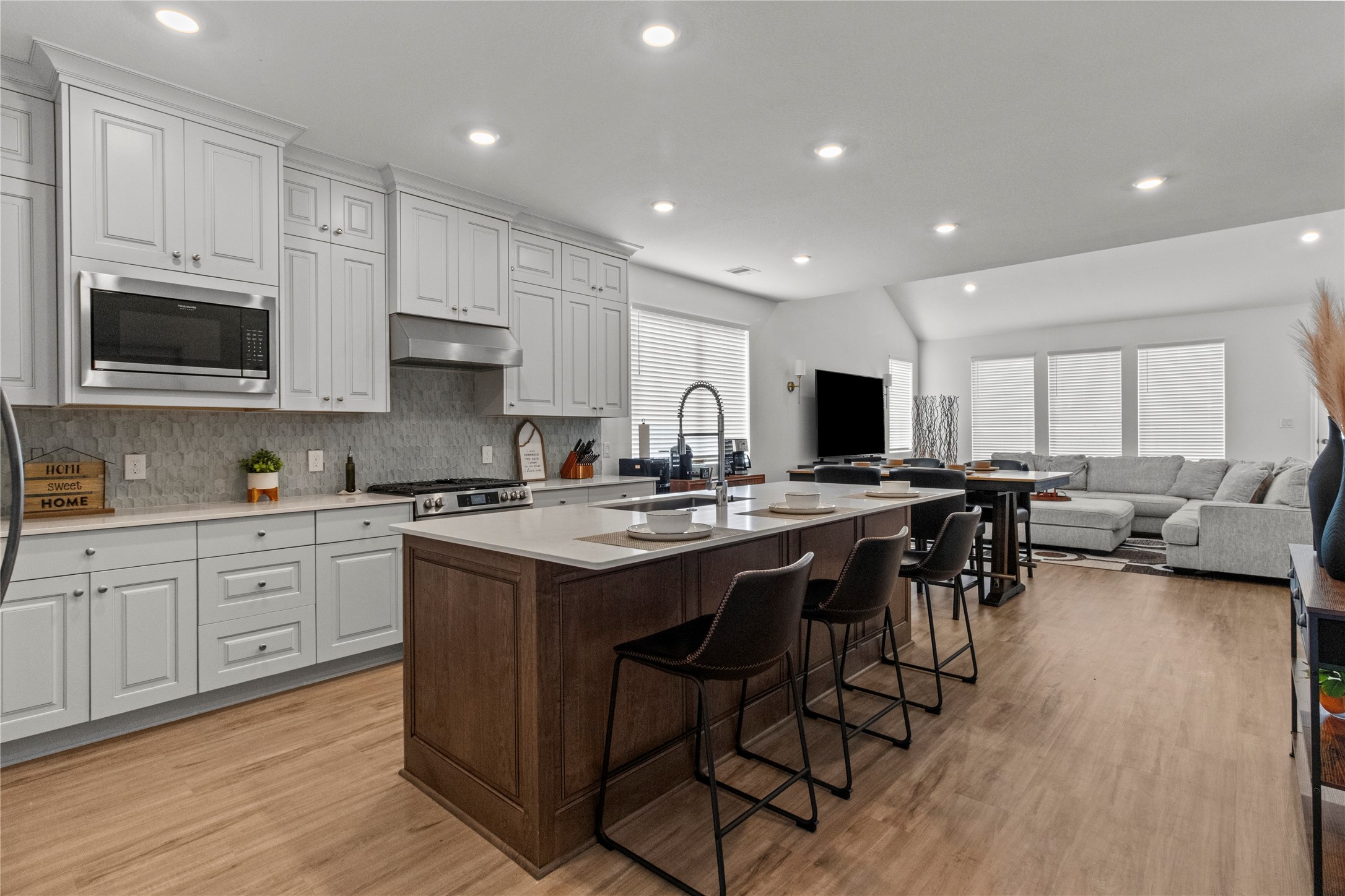Bright and spacious open-concept kitchen and living area featuring sleek white cabinetry, a large central island with seating, and modern stainless steel appliances. The adjacent living room offers ample natural light and a cozy seating arrangement, perfect for entertaining or relaxing.