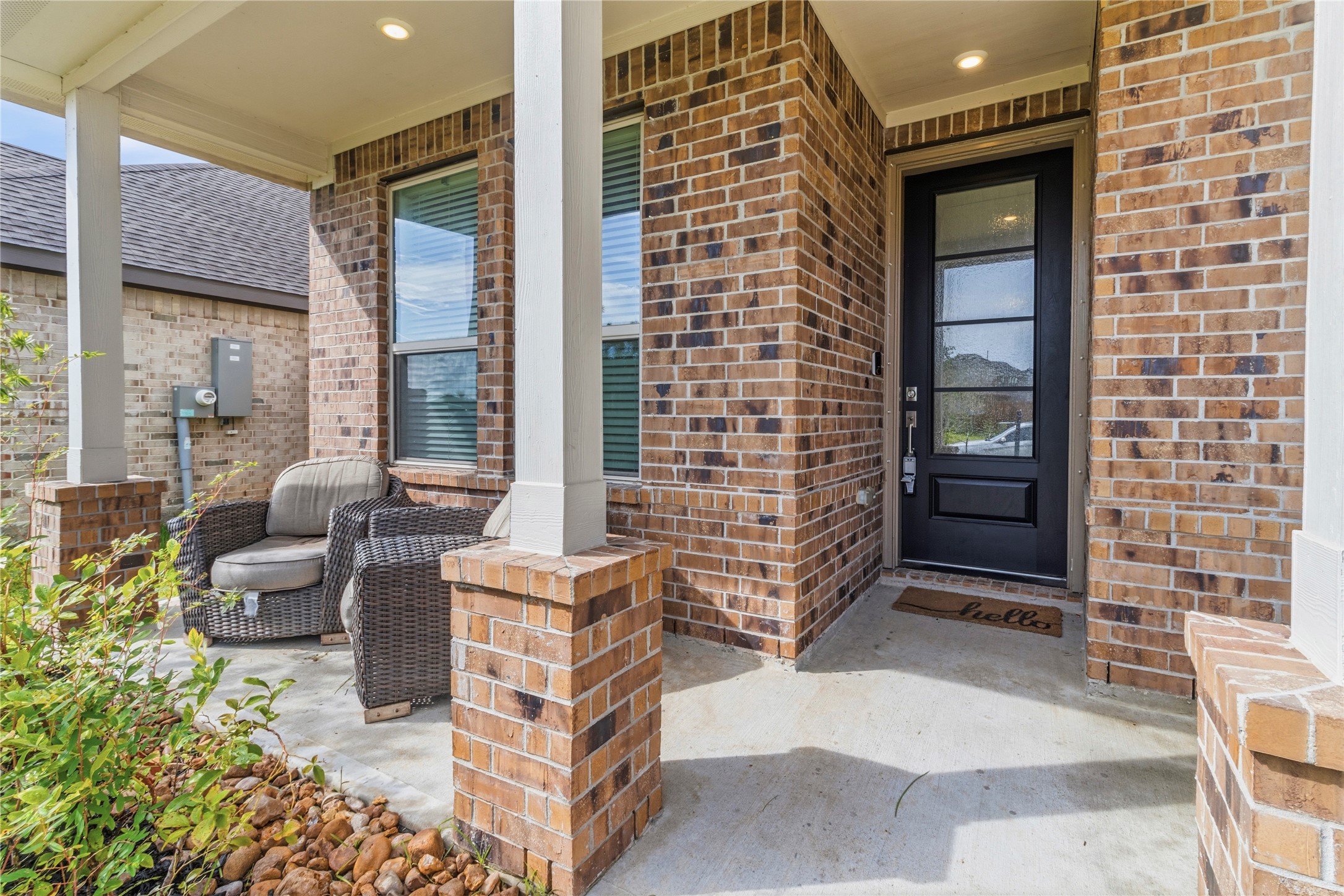 Charming brick front porch with cozy wicker seating and a welcoming entryway, perfect for relaxing and greeting guests.