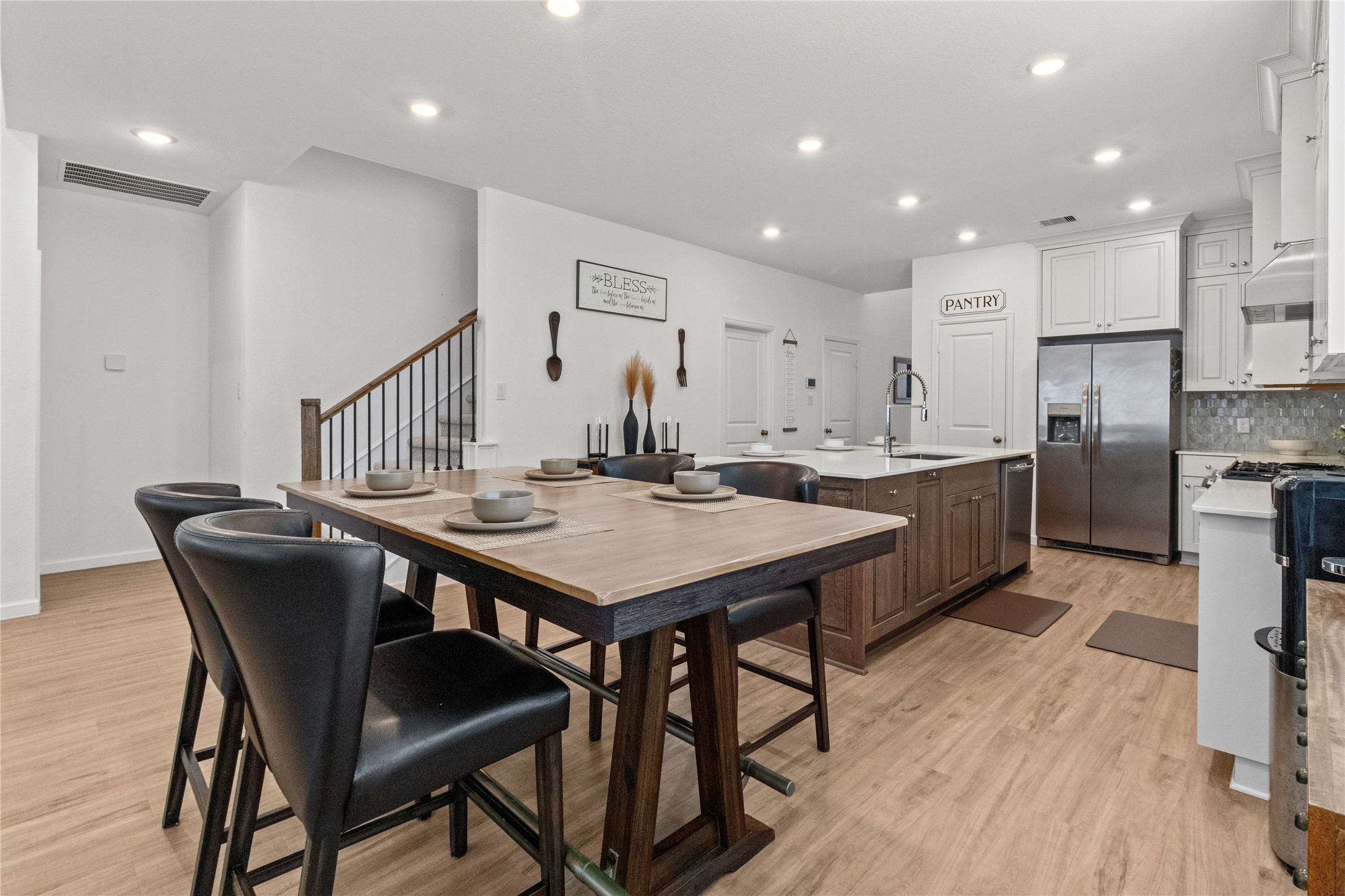 Bright and modern kitchen featuring a large center island with a farmhouse sink, sleek stainless steel appliances, and ample cabinetry, complemented by a stylish dining area with contemporary seating.