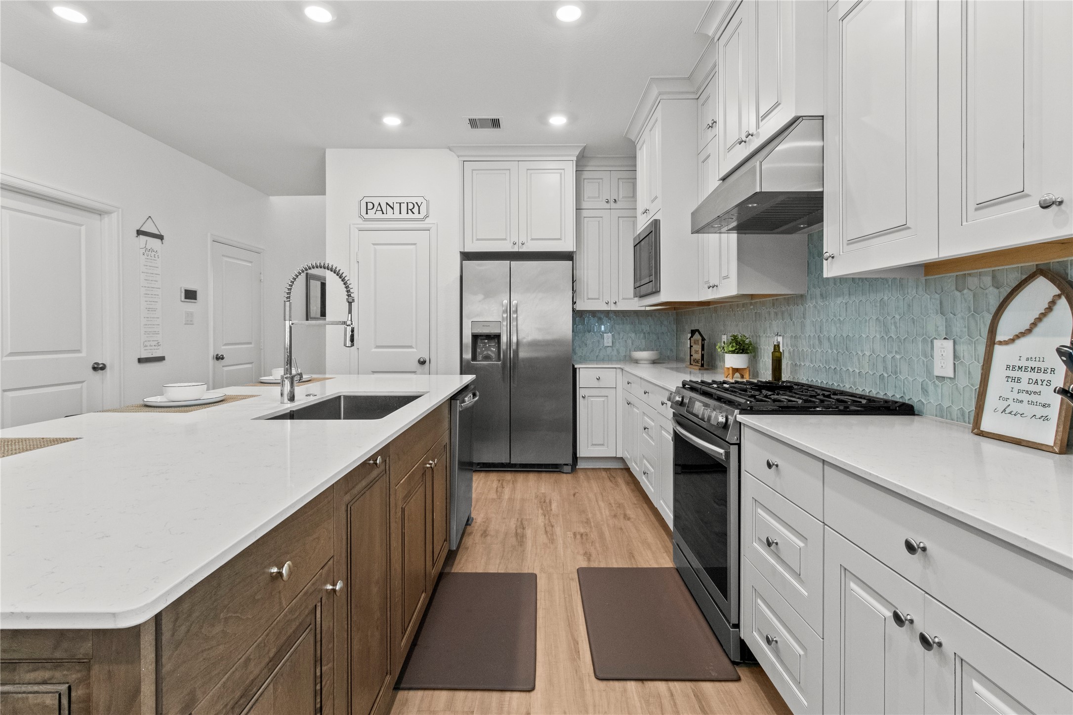 Sleek kitchen featuring a spacious island with a modern sink, stainless steel appliances, and ample cabinet space. The elegant backsplash and wood flooring add a warm touch to this inviting culinary space.