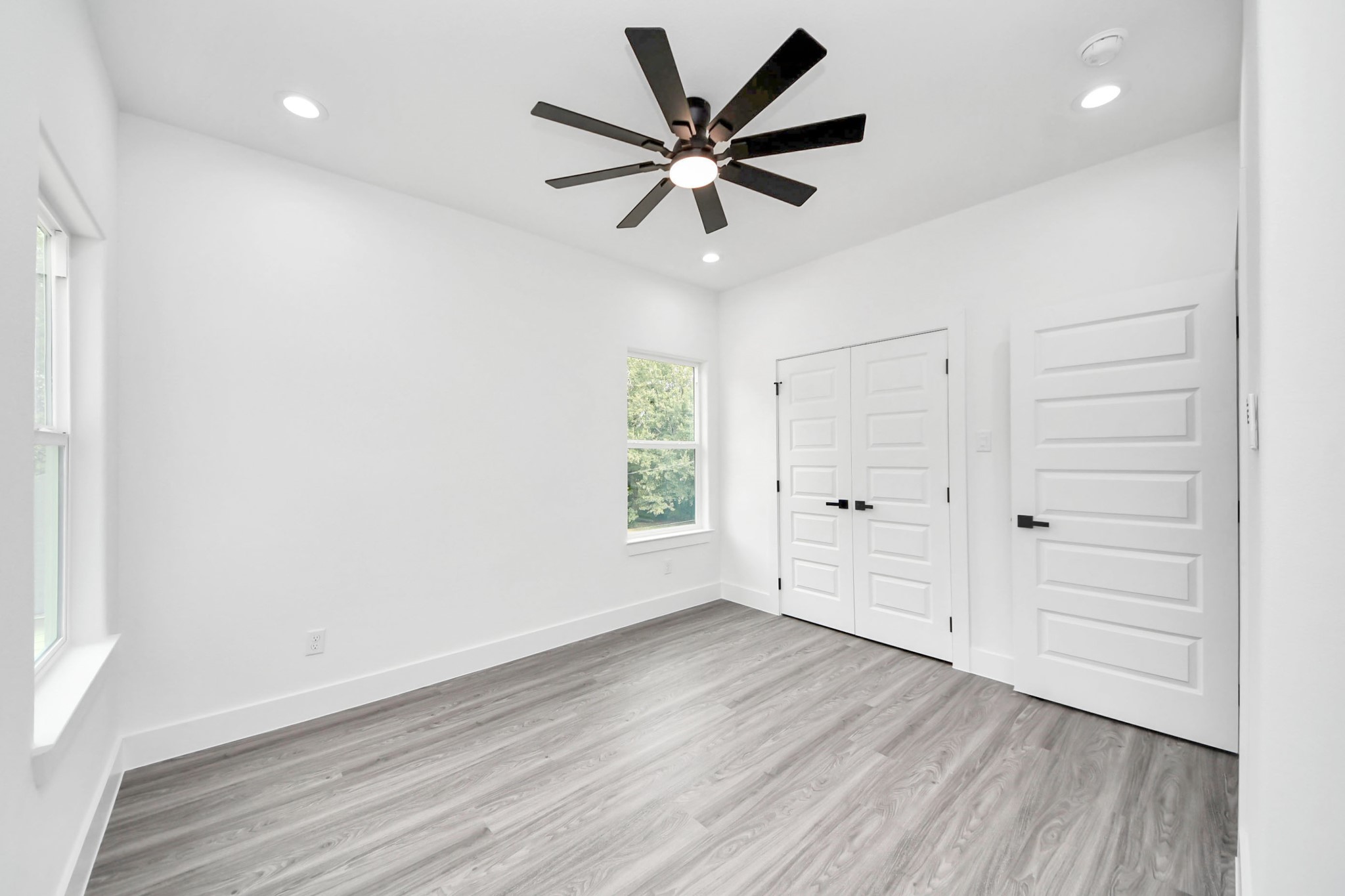 Bright and airy bedroom featuring modern wood flooring, a sleek ceiling fan, and ample natural light from large windows, creating a welcoming atmosphere.