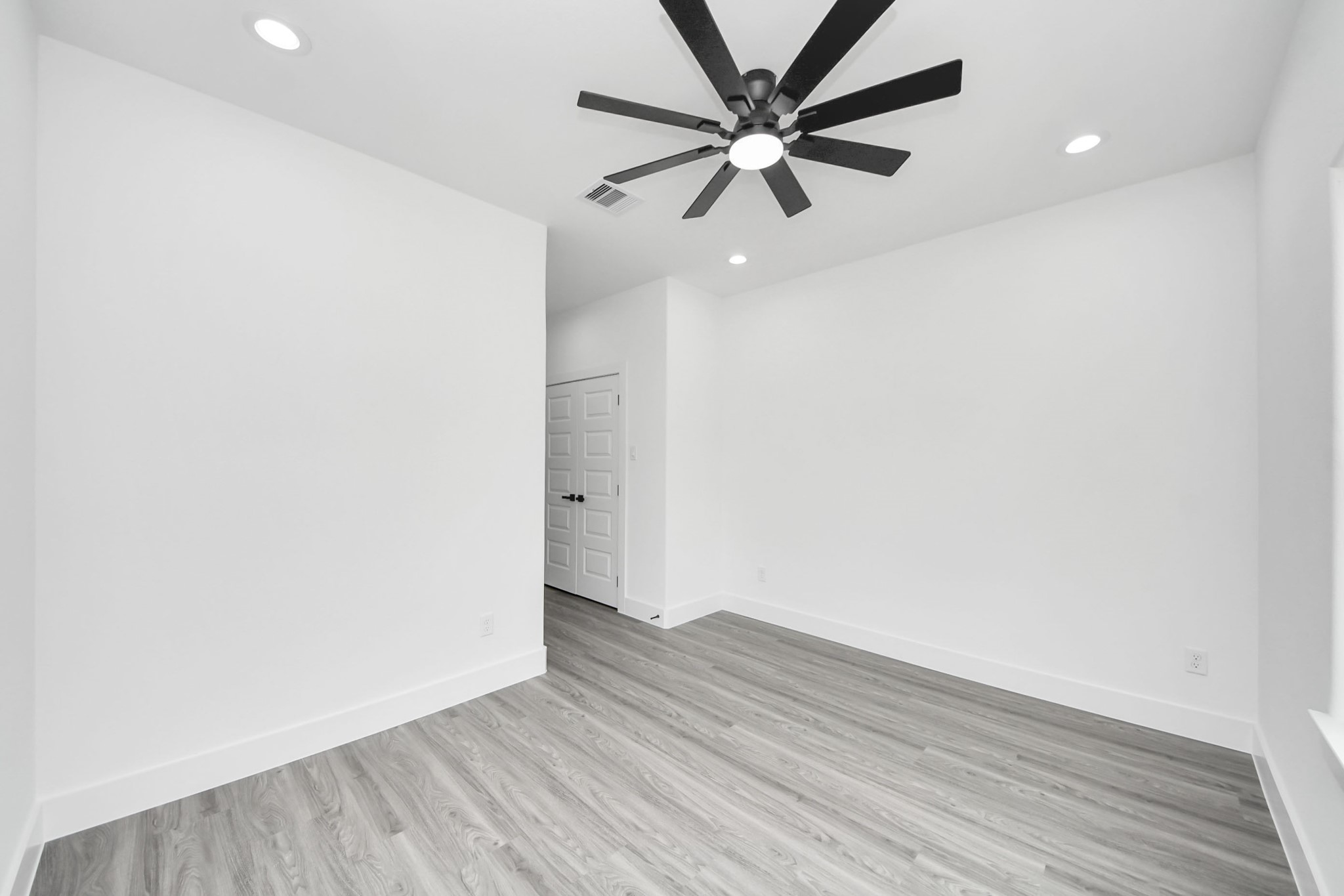 Bright, minimalist room featuring sleek wood flooring, recessed lighting, and a modern ceiling fan, perfect for a cozy and functional living space.