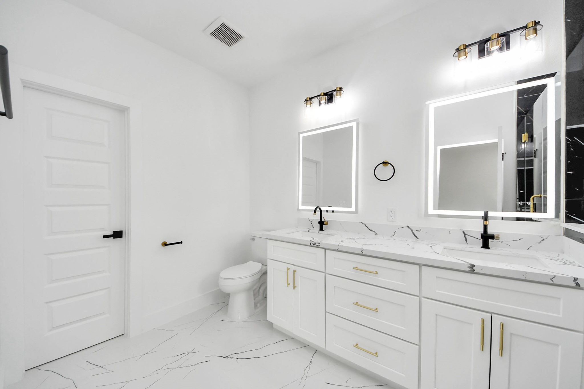 Sleek and modern bathroom featuring dual sinks with elegant marble countertops, illuminated mirrors, and stylish black fixtures.